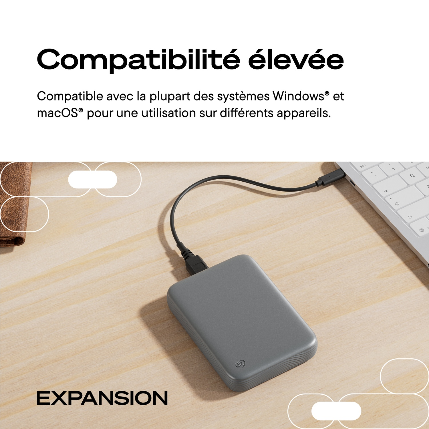 Un disque dur externe gris est relié par un câble à un ordinateur portable sur un bureau en bois.