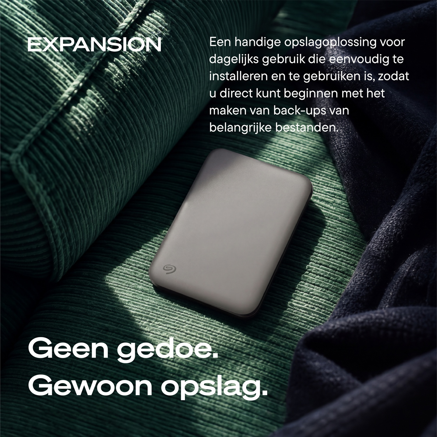 A dark external hard drive rests on a green corduroy sofa next to a dark blanket, with Dutch text.