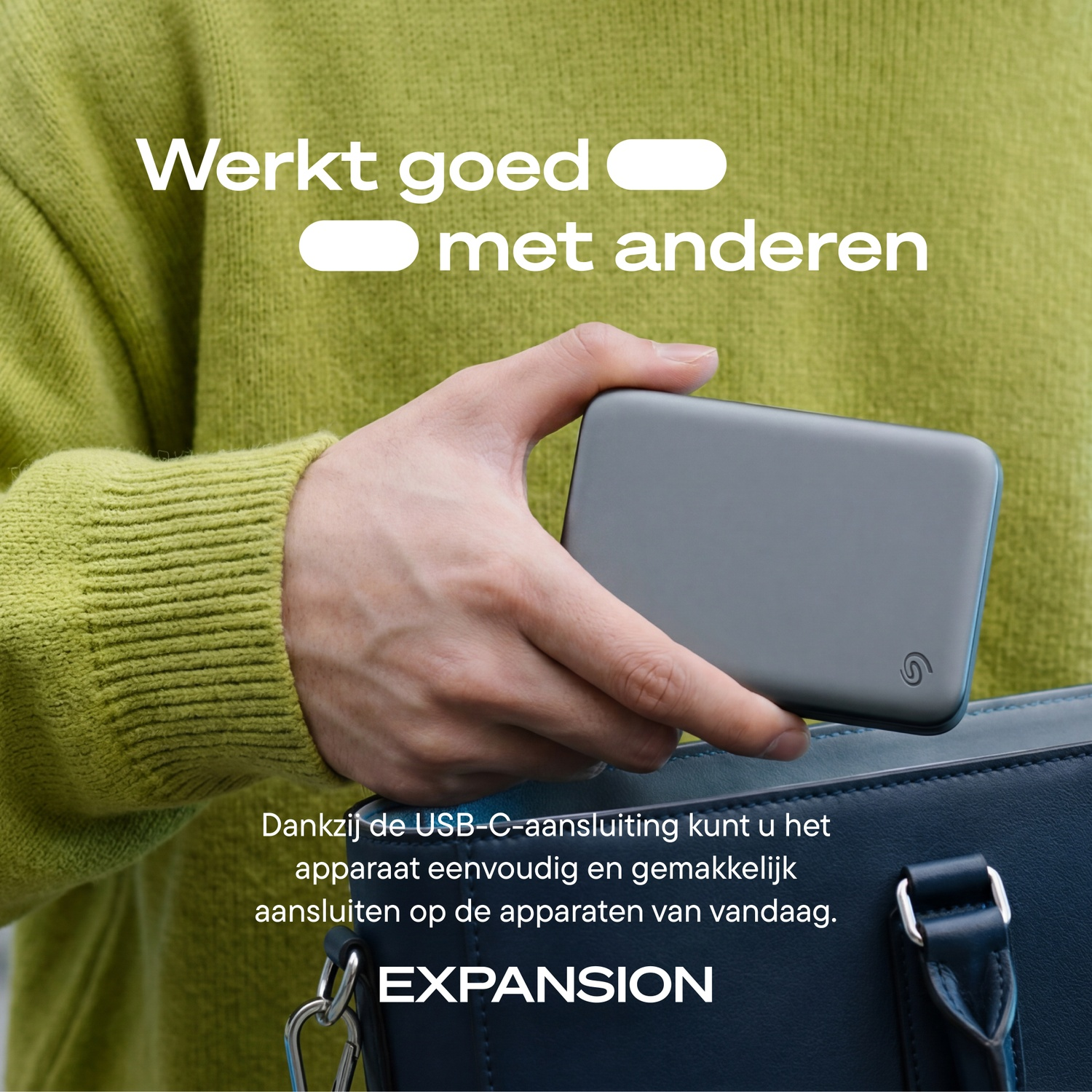 Person in green sweater puts gray external hard drive into blue bag.