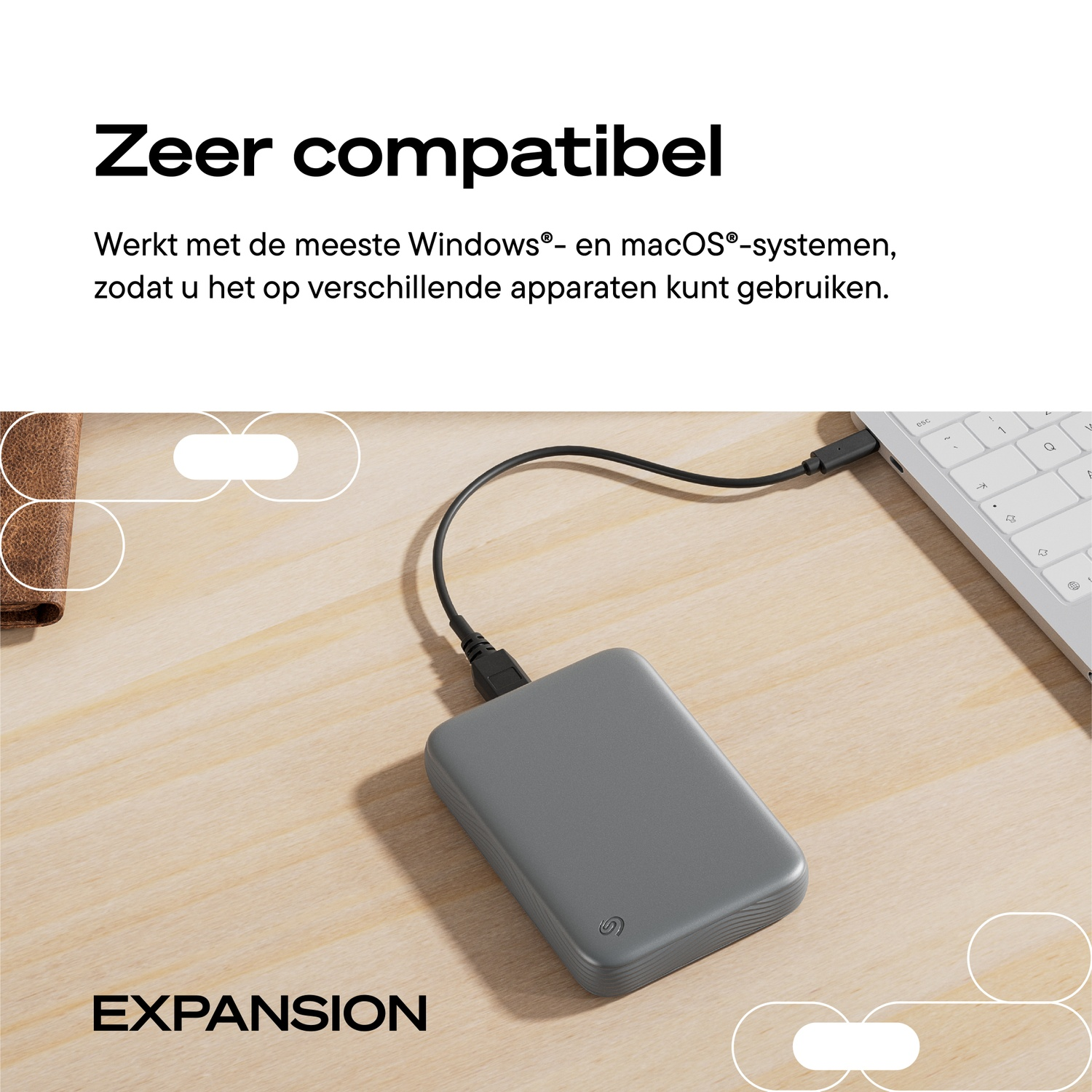 A gray external hard drive is connected by cable to a white laptop on a wooden surface.