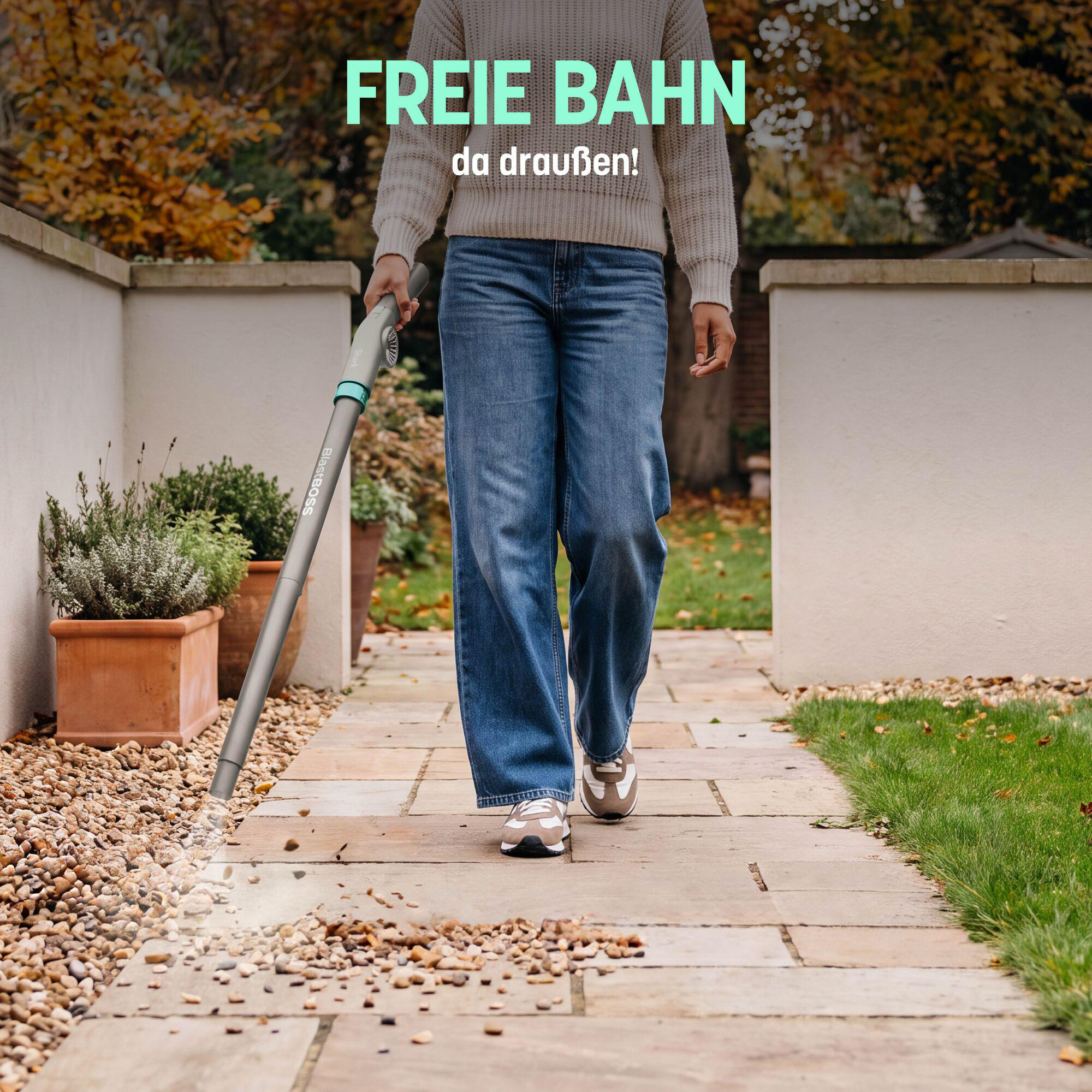 Eine Person nutzt einen grauen Laubsauger auf einem Steinweg im Garten.