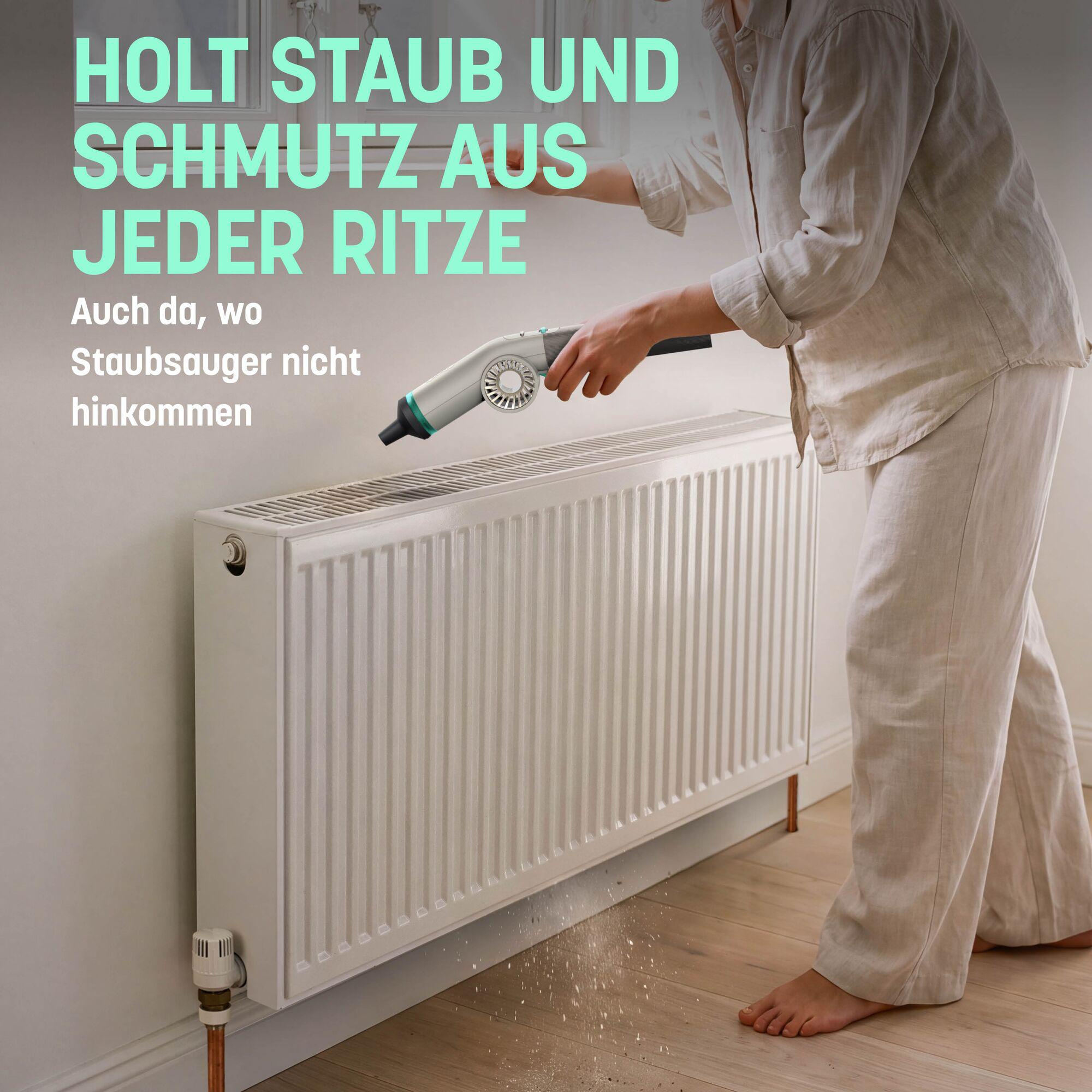 Person reinigt einen weißen Heizkörper mit einem kleinen Handstaubsauger, Schmutz fällt auf den Holzboden.