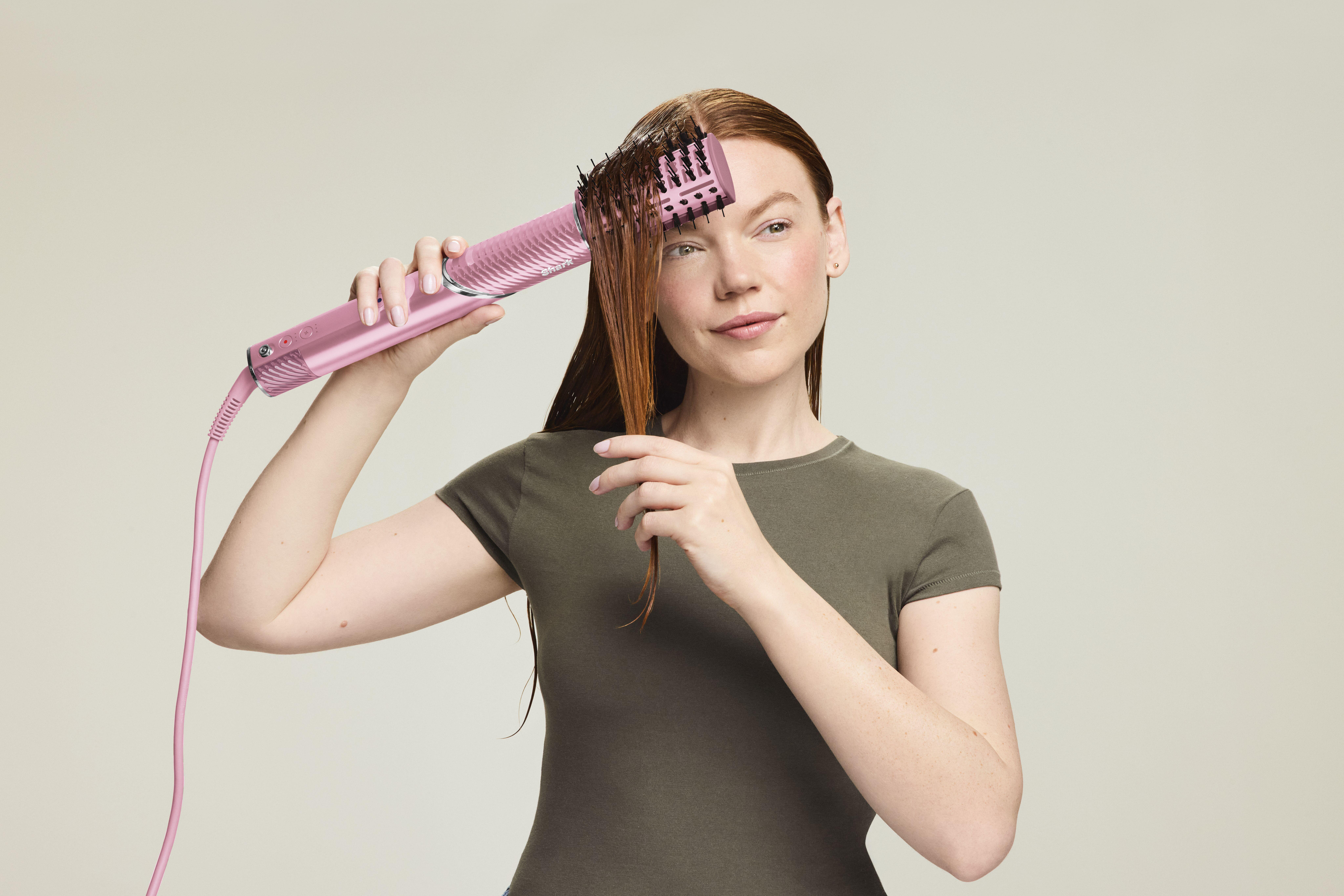 Frau in grauem Shirt nutzt eine pinke Warmluftbürste zum Haareglätten.