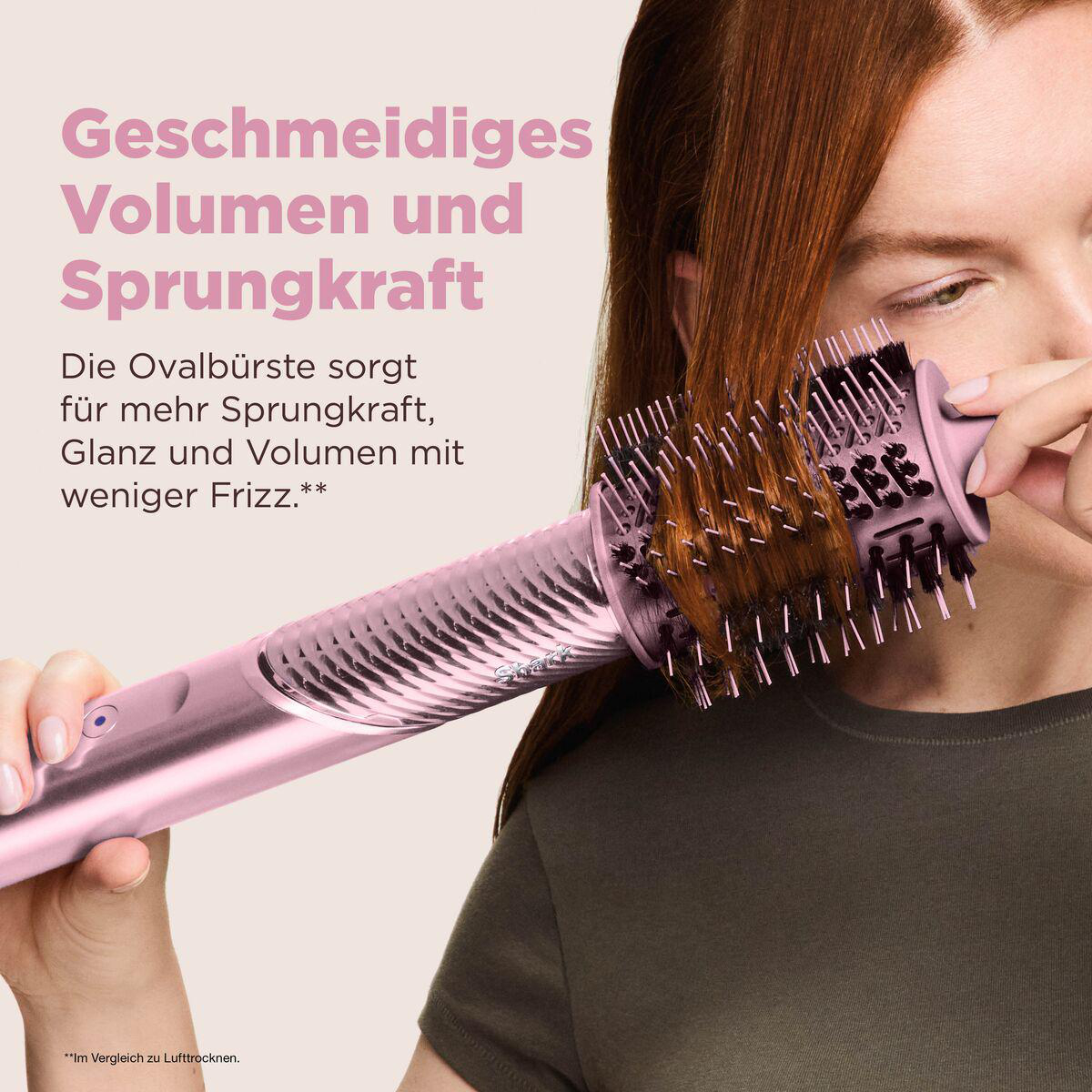 Eine Frau stylt ihr rotes Haar mit einer rosa Heißluftbürste. Deutscher Text wirbt für Volumen.