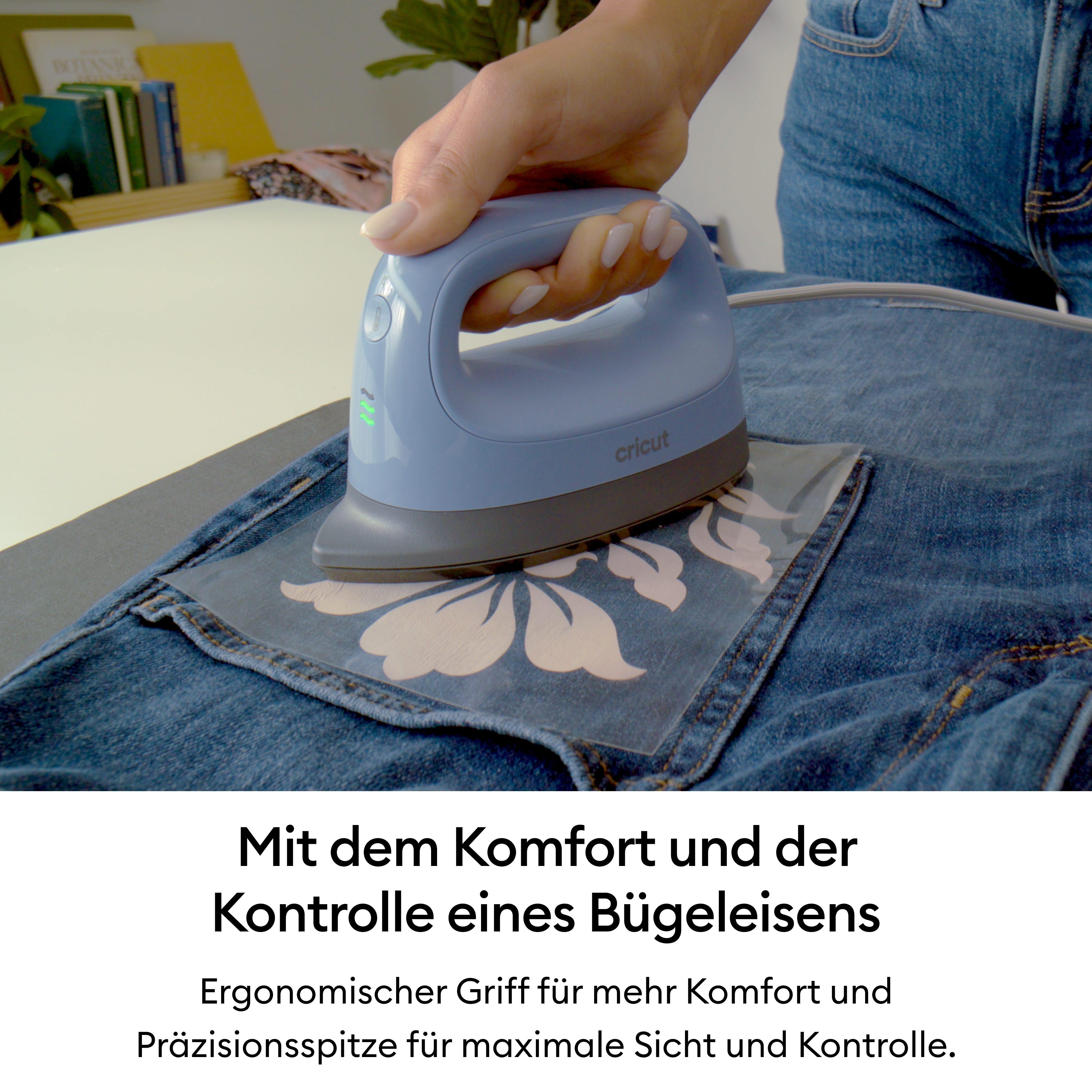 Person bügelt ein florales Design auf Jeansstoff mit einem blauen Handbügeleisen.