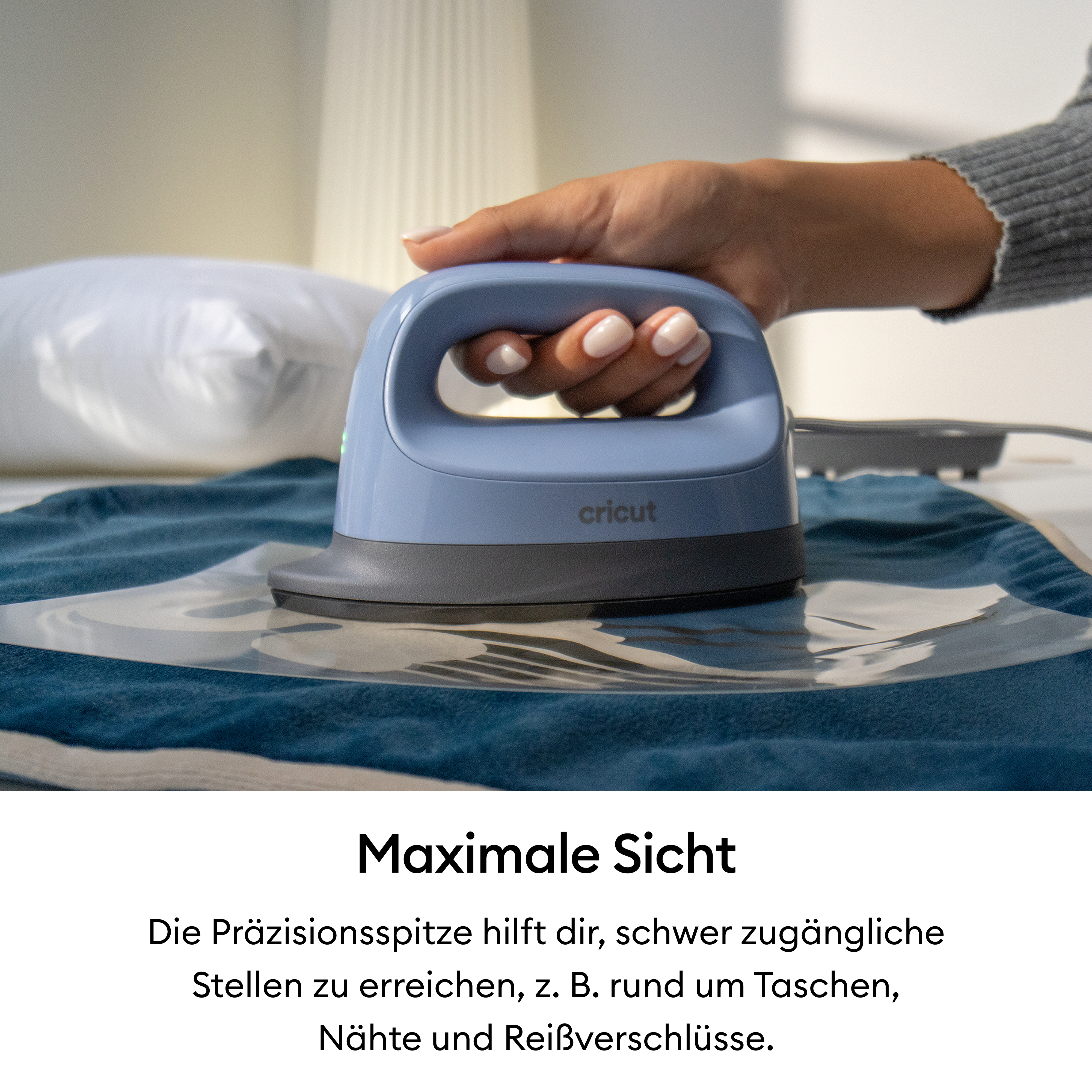 Eine Hand hält eine hellblaue Cricut Easypress Mini, die auf einer blauen Textilie mit Folie liegt.