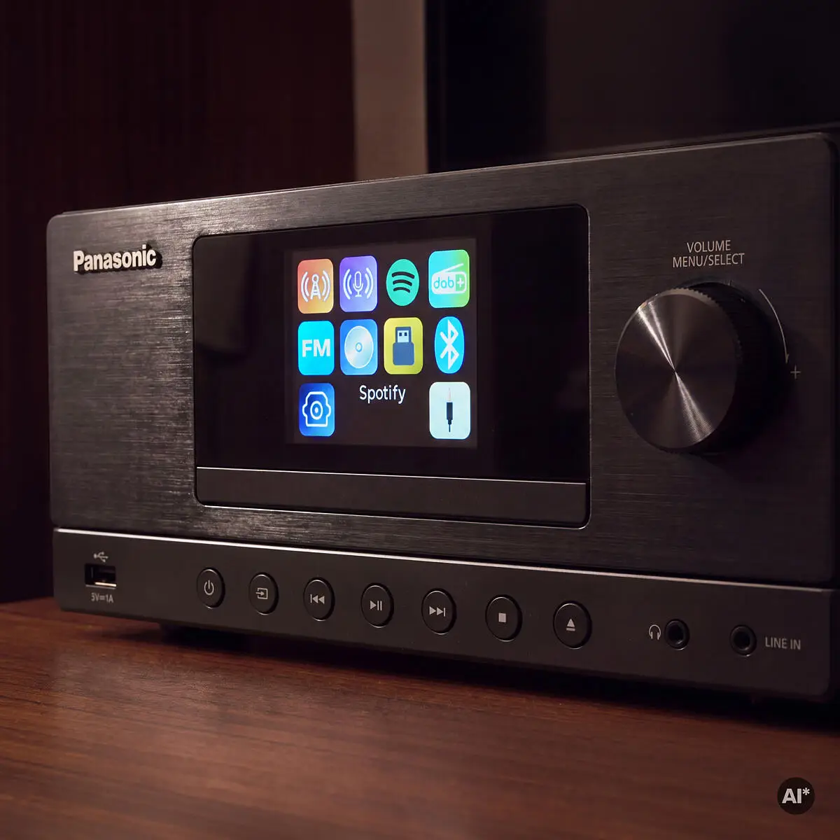 Egy Panasonic audio vevő színes kijelzővel és média opciókkal fa asztalon.
