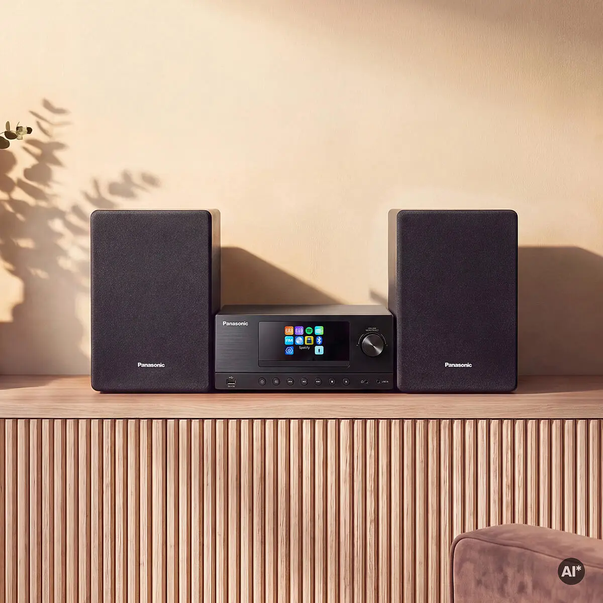 Fekete Panasonic audiorendszer két hangszóróval egy fa asztalon, bézs fal előtt.