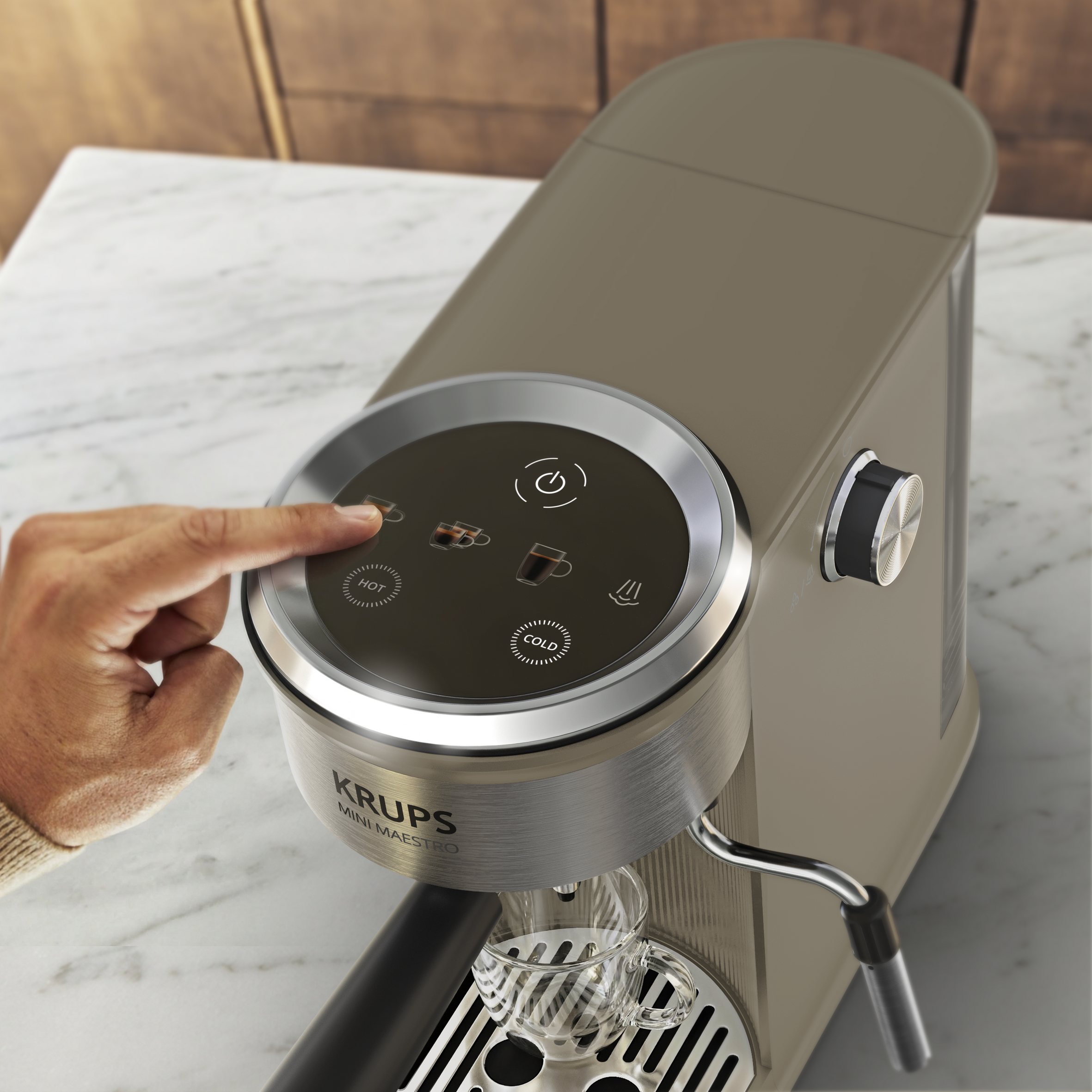 Una mano opera la pantalla táctil de una cafetera Krups Mini Maestro beige en una encimera de mármol.