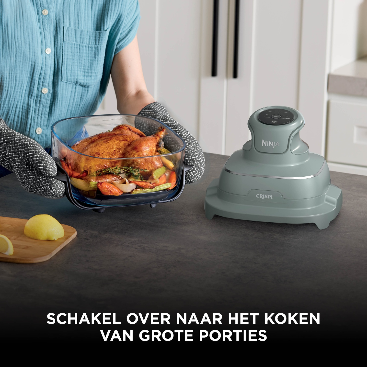 A person holds a glass dish with roasted chicken and vegetables beside a Ninja appliance.