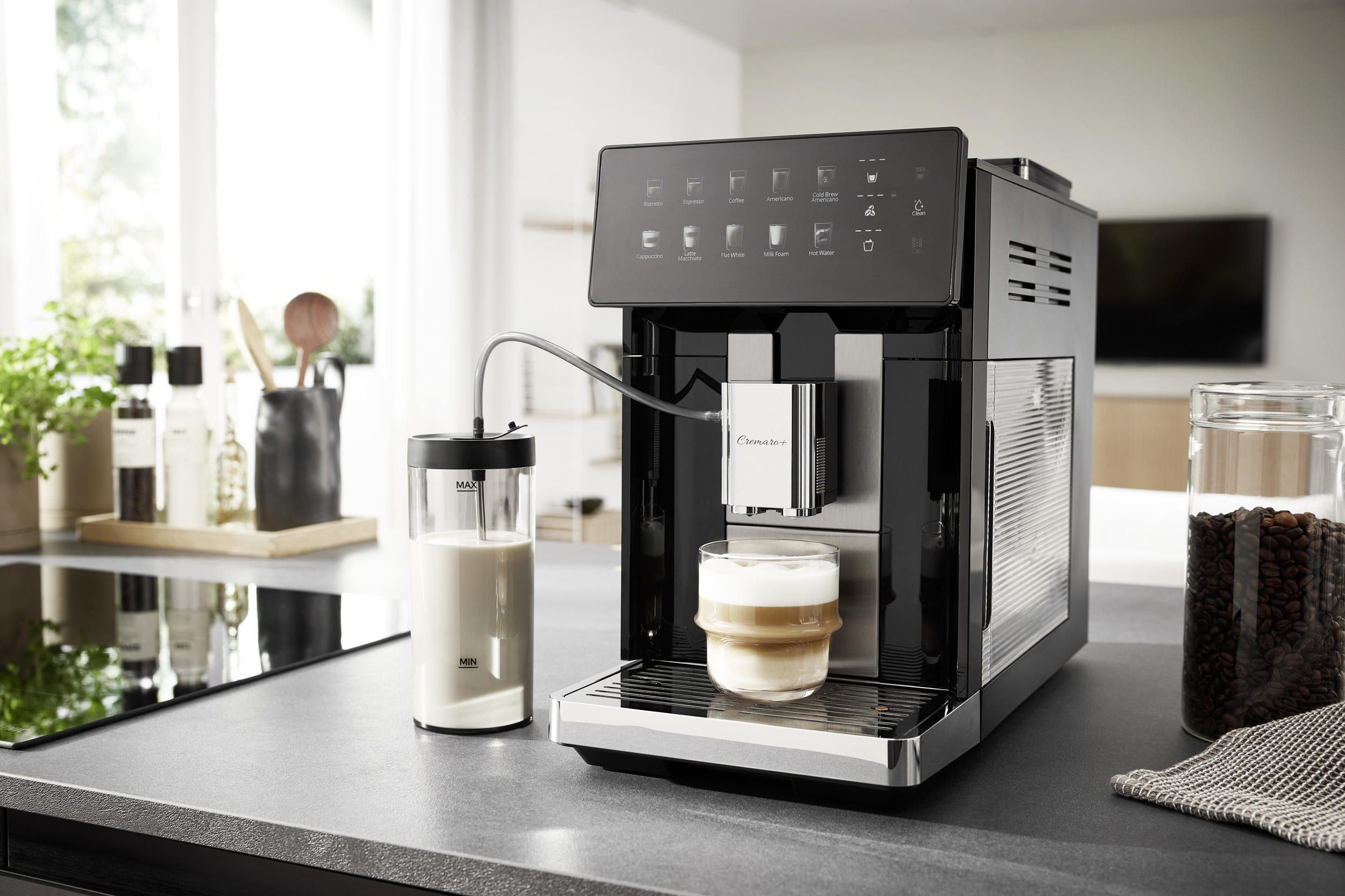 Moderna macchina da caffè nera su un piano cucina con contenitore del latte, tazza di vetro e barattolo.