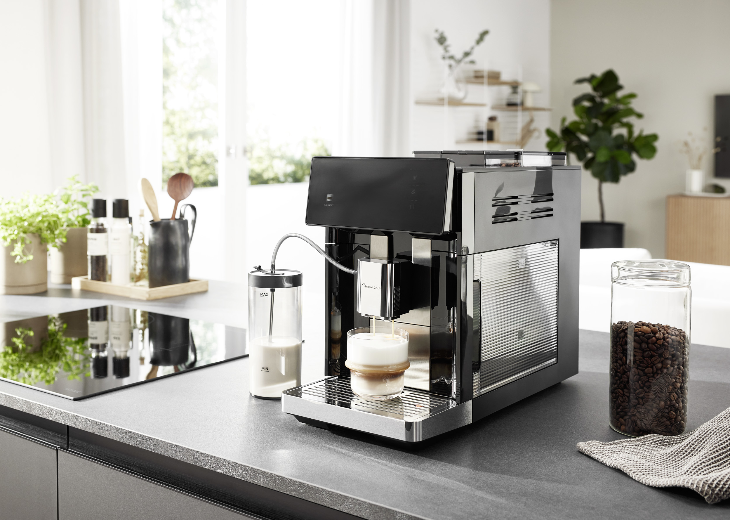 Una macchina da caffè nera versa un cappuccino a strati in un bicchiere sul bancone della cucina.