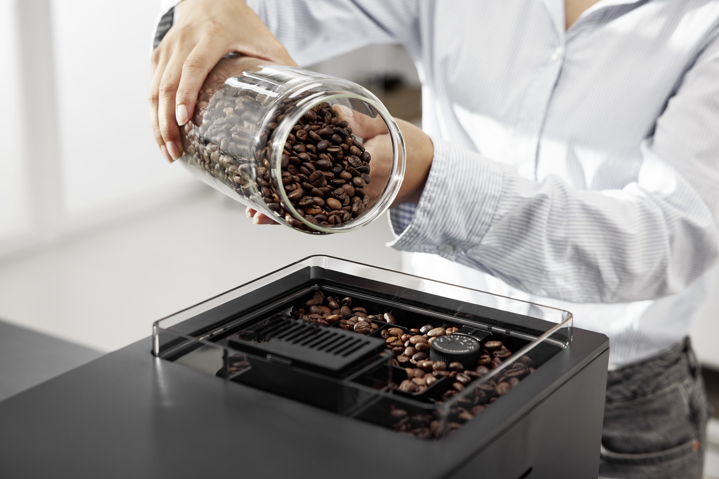 Una persona versa chicchi di caffè da un barattolo di vetro nella tramoggia di una macchina da caffè.