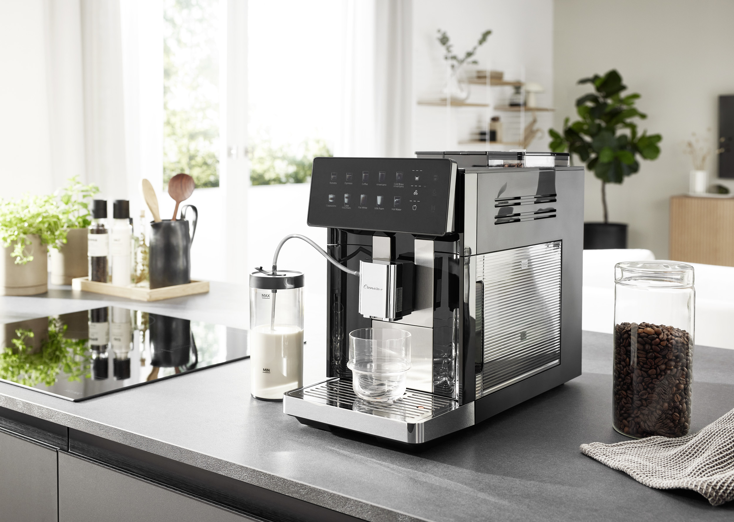 Macchina da caffè nera con contenitore del latte e bicchiere su un bancone, vicino a un barattolo di caffè.