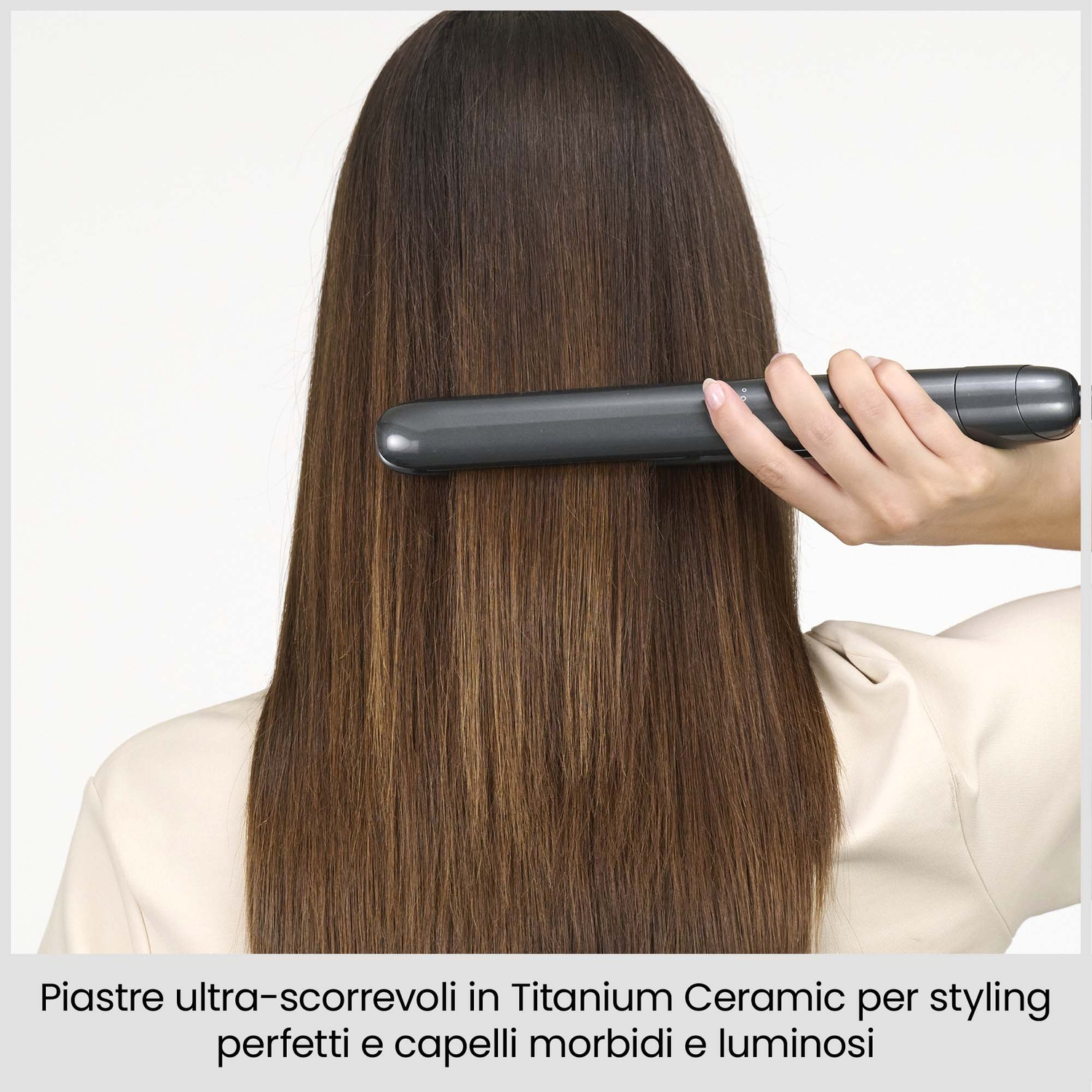 Una donna usa una piastra per capelli grigia sui suoi lunghi capelli castani.