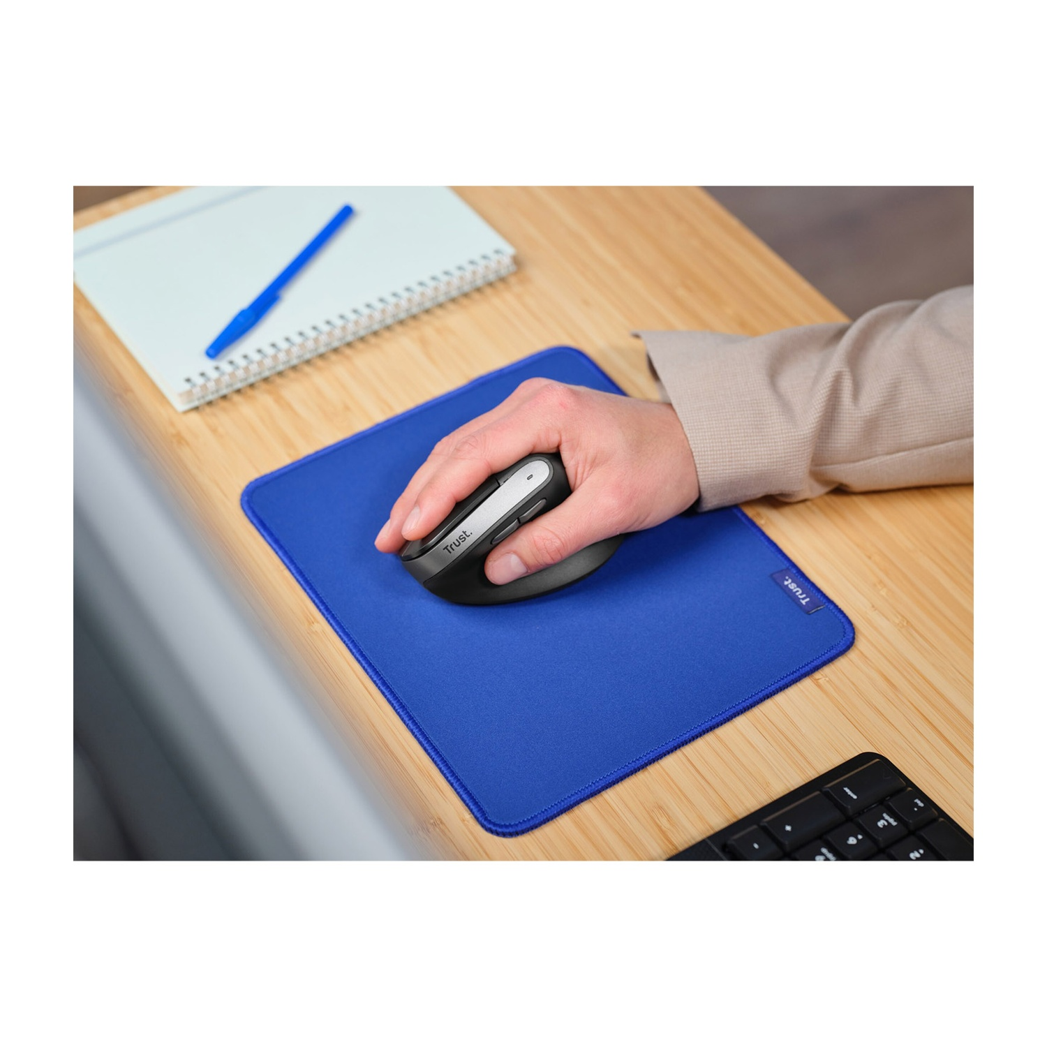 Mano che usa un mouse ergonomico Trust su un tappetino blu.