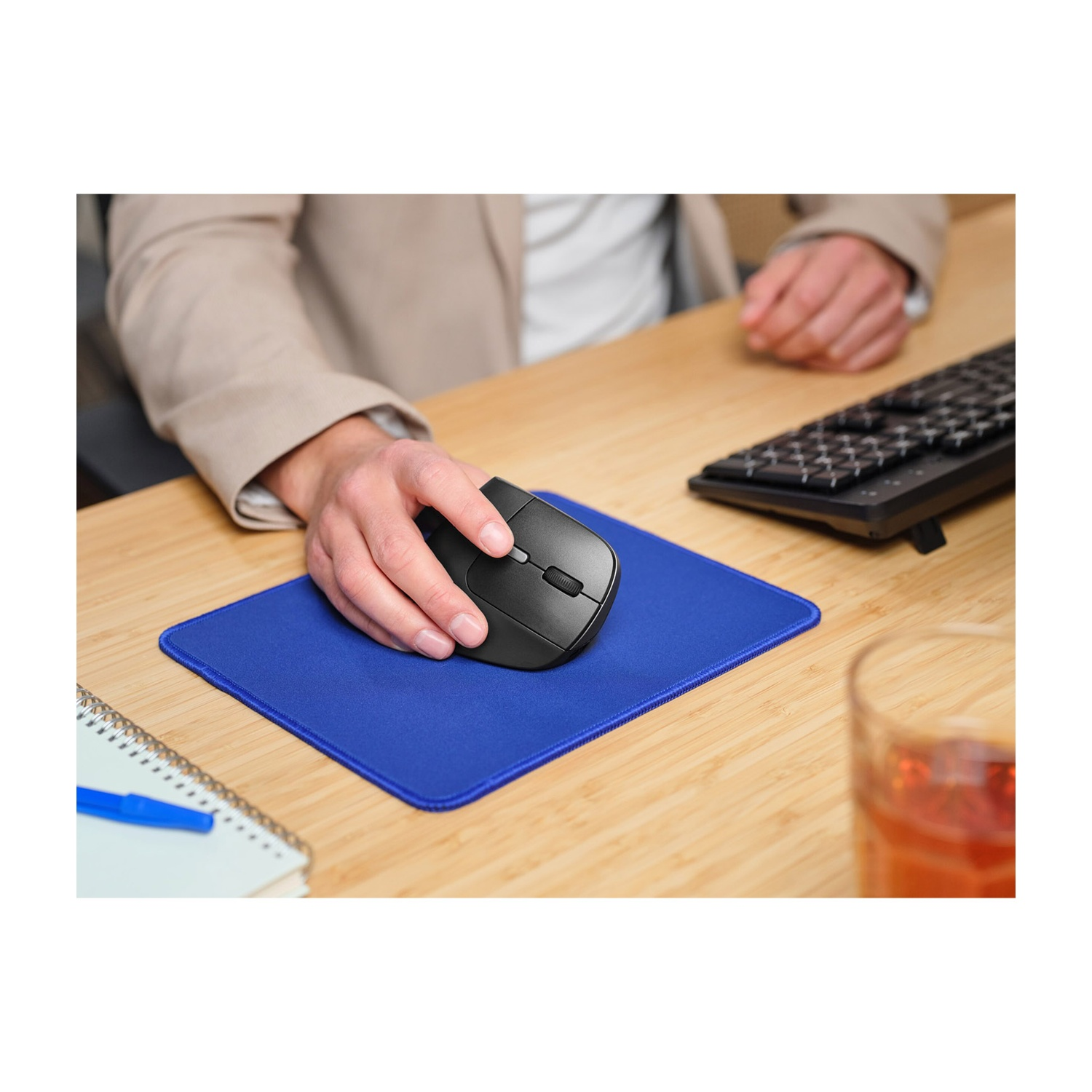Una persona a una scrivania di legno usa un mouse nero su un tappetino blu.