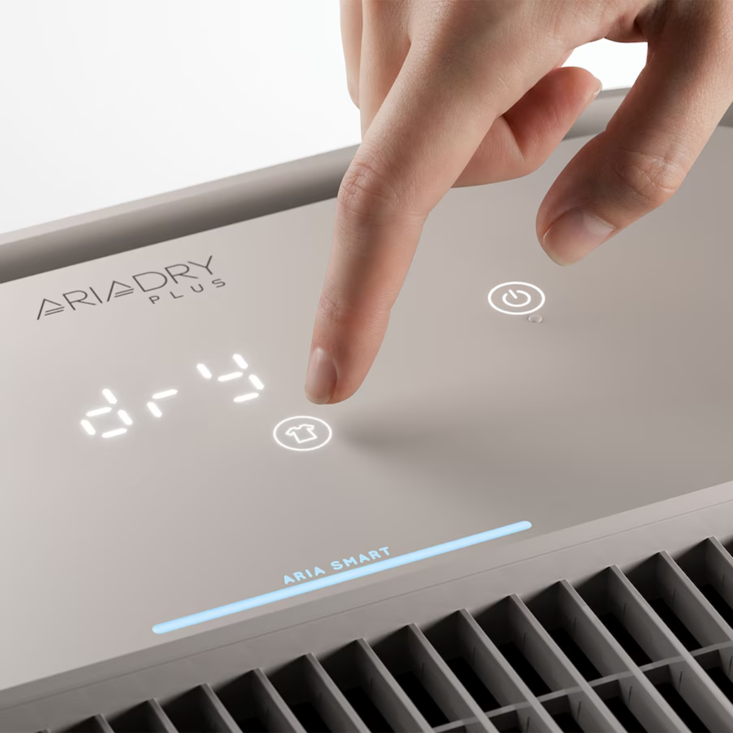 Un dedo toca un botón iluminado en el panel de control de un deshumidificador Aria Dry Plus.