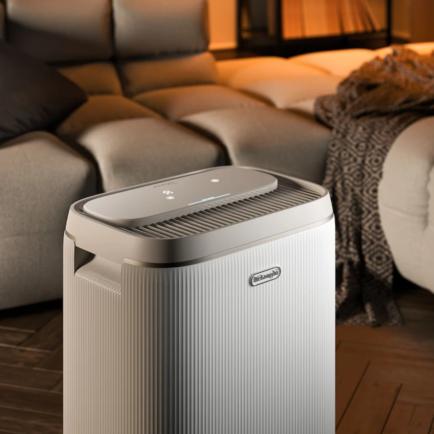Un aparato blanco De'Longhi se encuentra en una sala frente a un gran sofá.