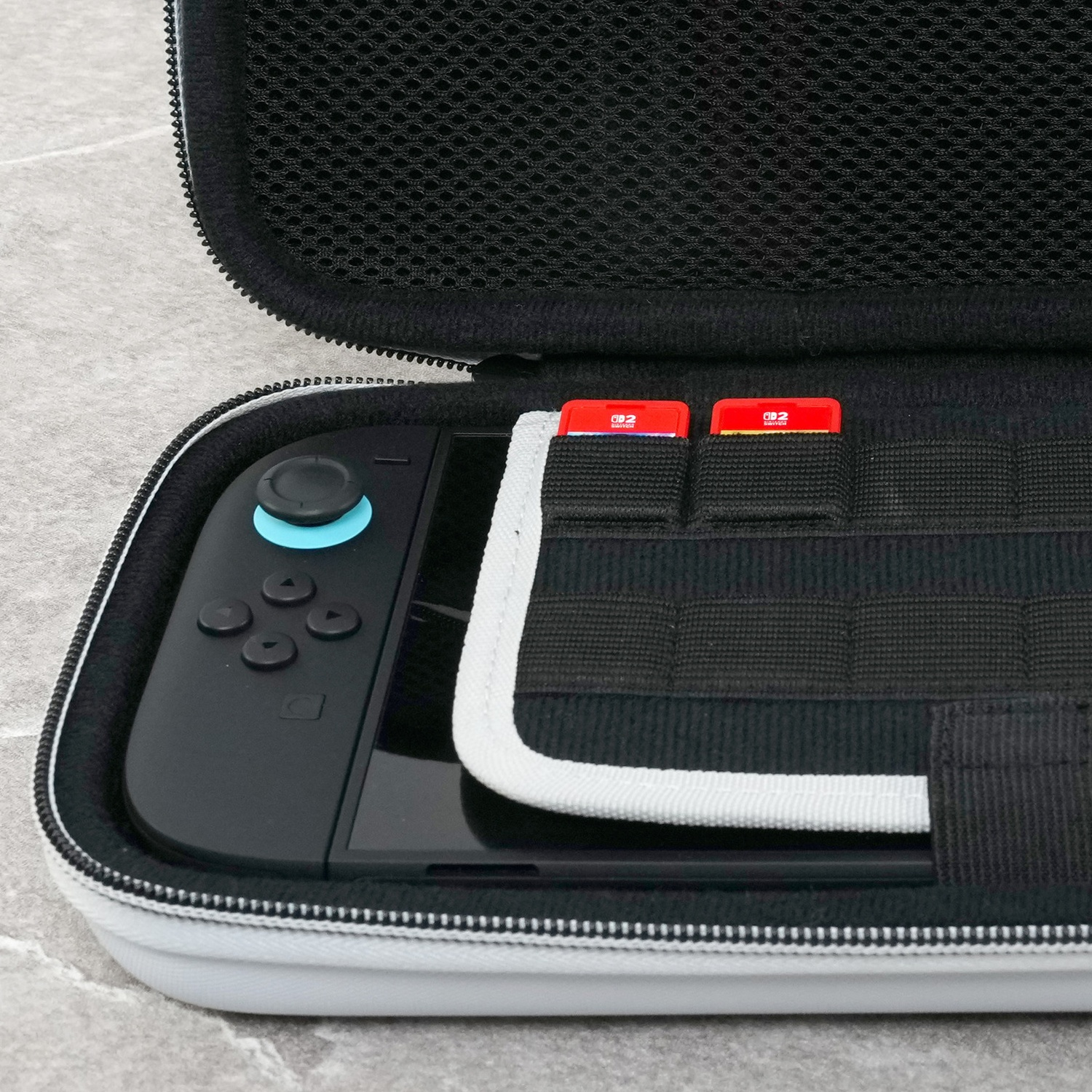 An open black and white case contains a black gaming console and two red game cartridges.