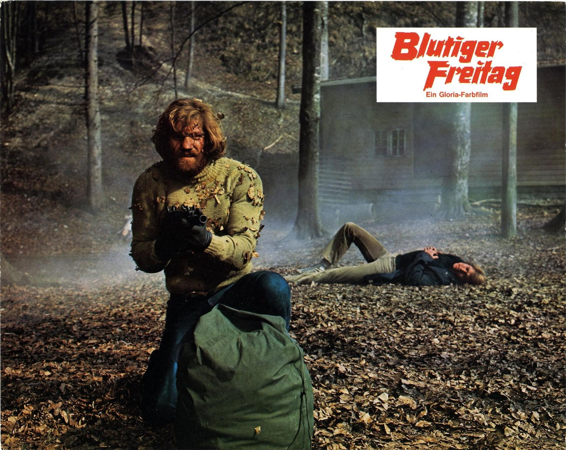 Ein bewaffneter Mann kniet im Wald neben einer Leiche vor einer Holzhütte, Titeltext Blutiger Freitag.