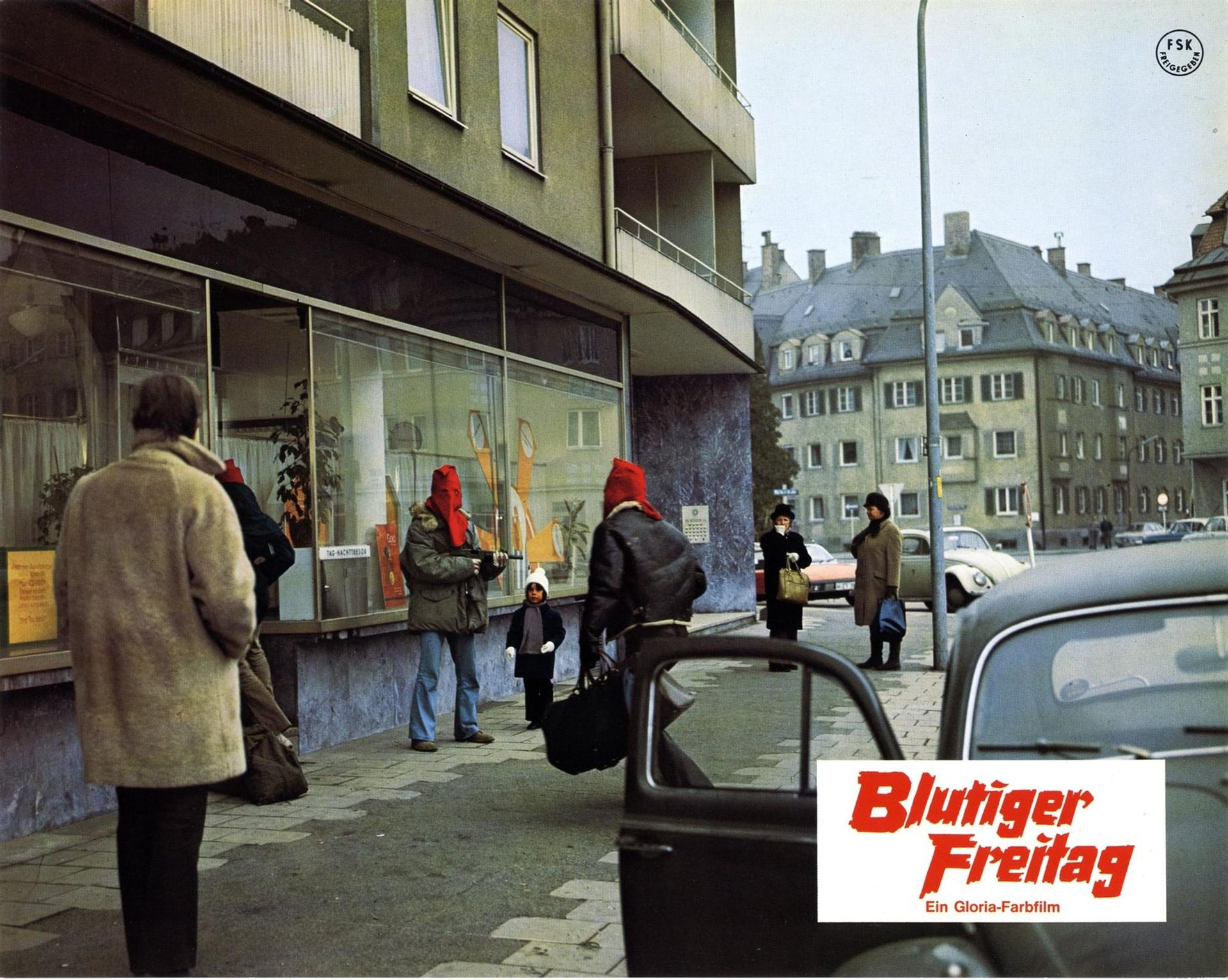 Szene aus Blutiger Freitag mit bewaffneten Männern mit roten Kapuzen und einem Kind auf der Straße.