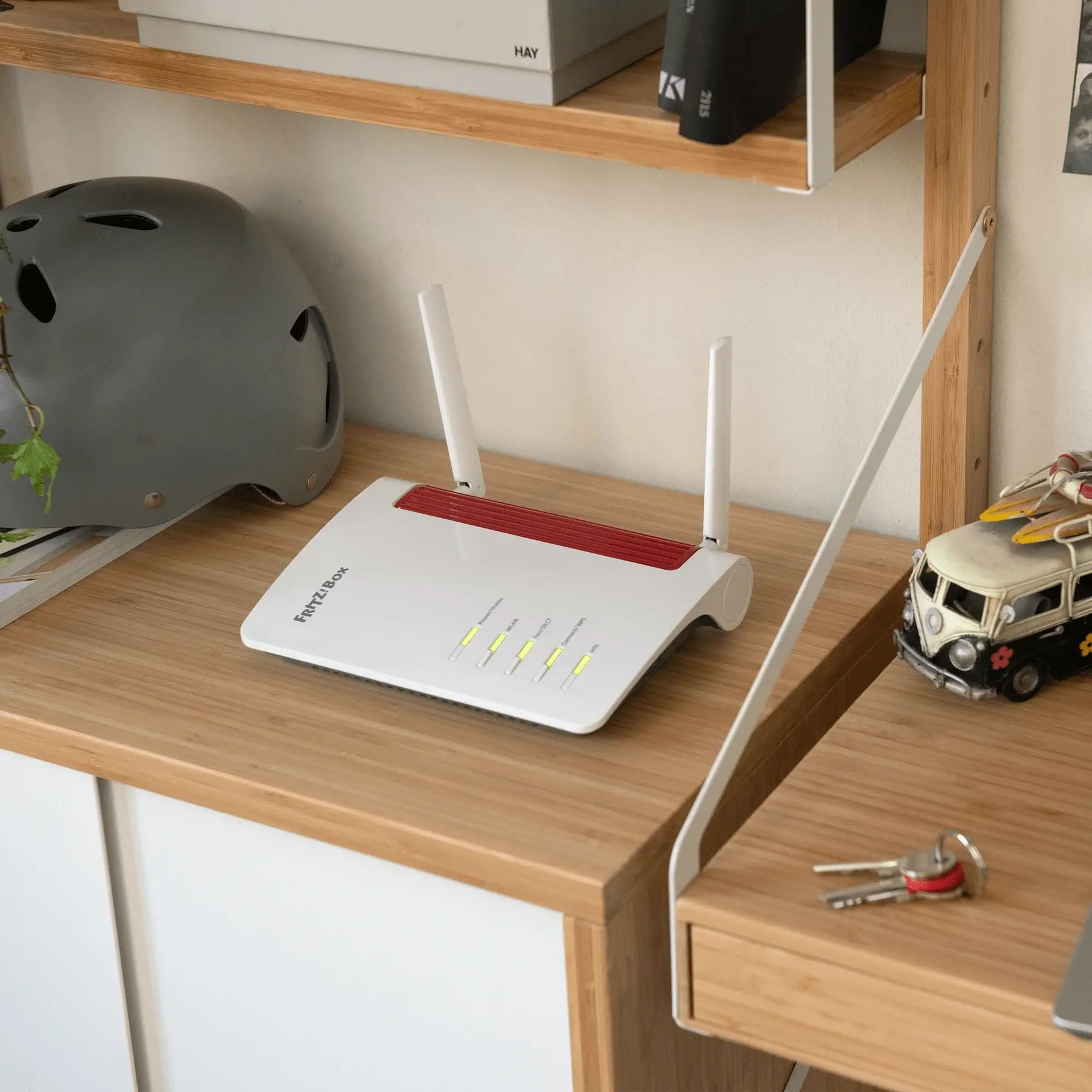 Ein weißer WLAN-Router mit zwei Antennen steht auf einem Holzregal, neben einem grauen Helm und einem Spielzeug-Bus.