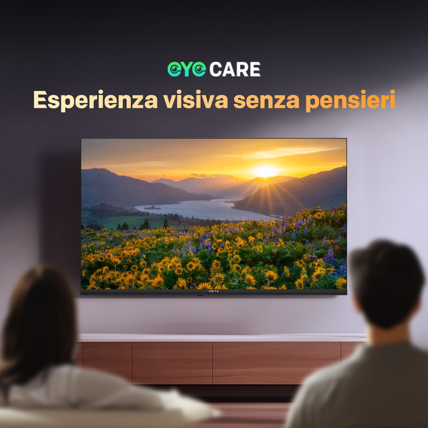 Due persone guardano una grande TV con un paesaggio di montagna e girasoli.