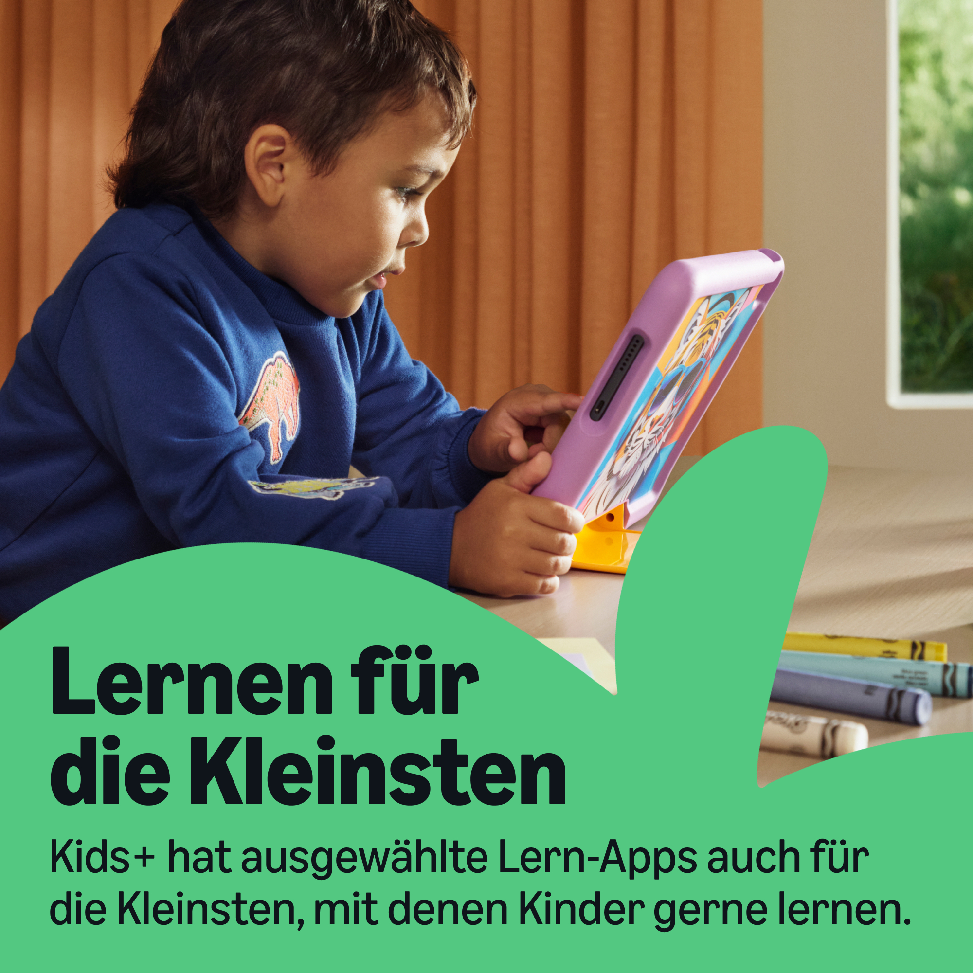 Ein Kind in einem blauen Pullover sitzt am Tisch und bedient ein pinkes Tablet.