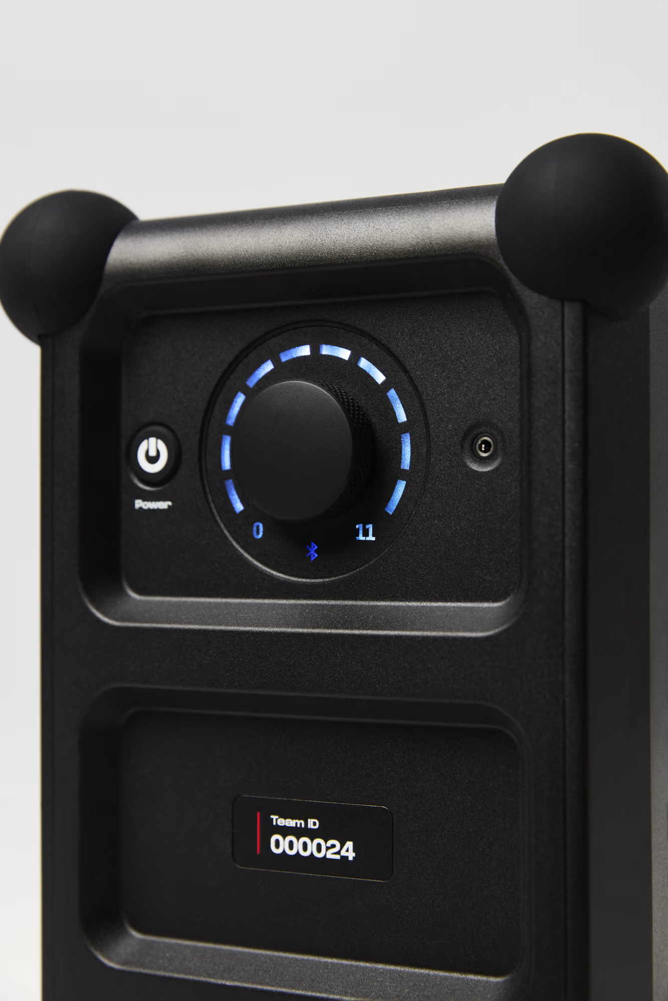 Schwarzes elektronisches Gerät mit blauem LED-Drehregler, Power-Taste und Team-ID-Display auf weißem Hintergrund.