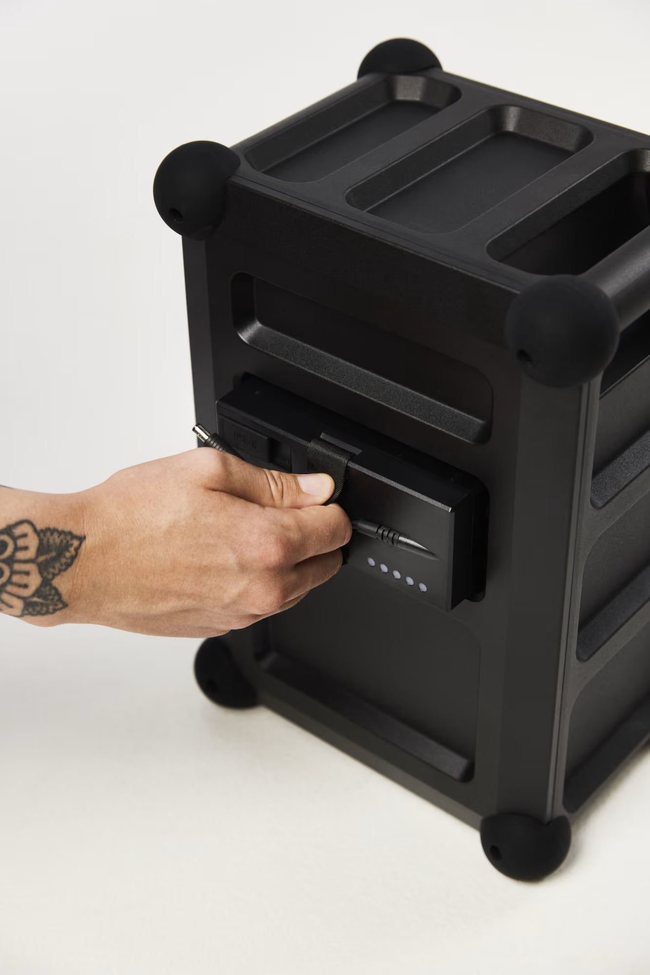 Eine tätowierte Hand zieht eine schwarze Batterie aus einem schwarzen Lautsprecher.