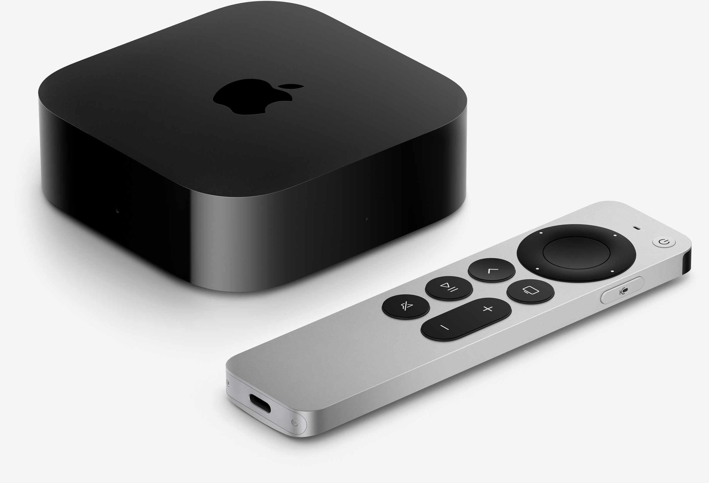 Fekete Apple TV doboz és ezüst Siri Remote fekete gombokkal fehér háttér előtt.