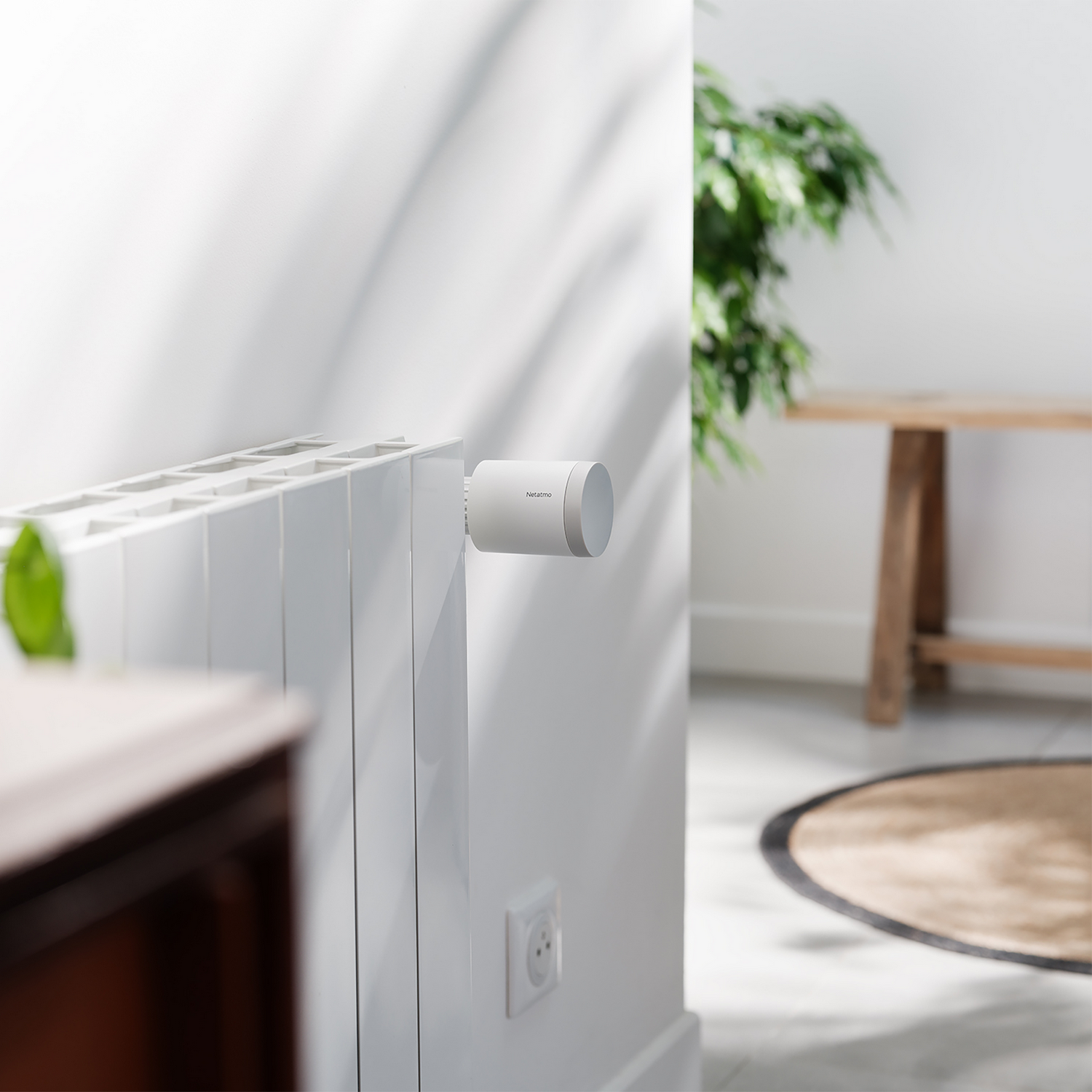 Una válvula de radiador inteligente blanca Netatmo está instalada en un radiador blanco en una habitación iluminada.