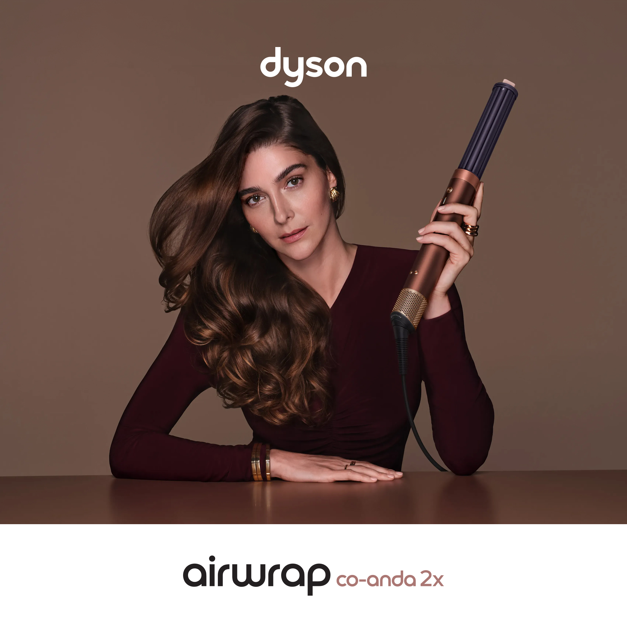 Kobieta z brązowymi włosami trzyma Dyson Airwrap na brązowym tle.