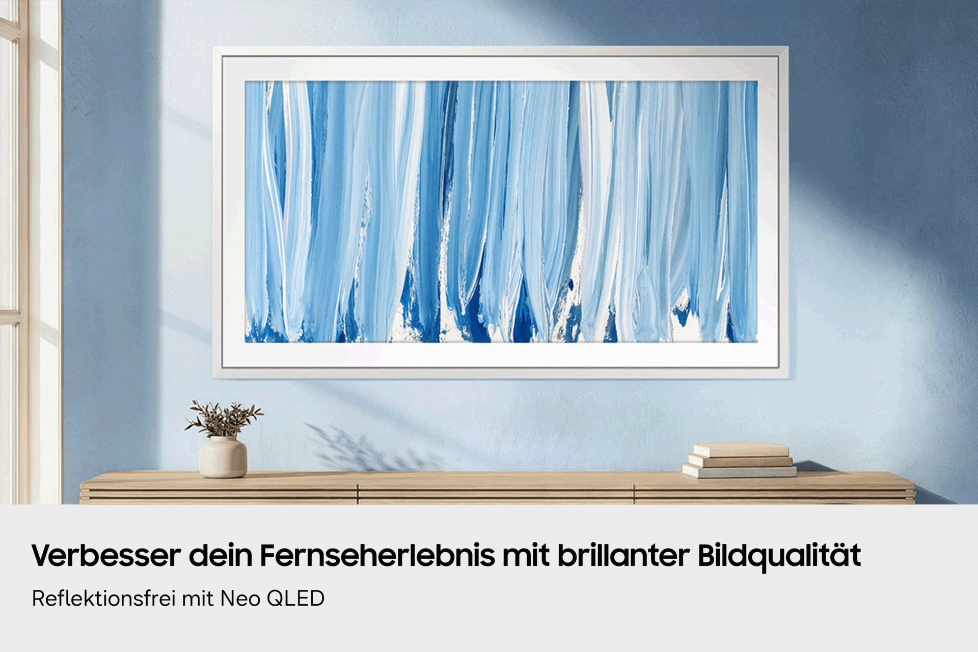 Ein rahmenloser Fernseher mit blauem Kunstbild an einer hellblauen Wand über einem Holzschrank.