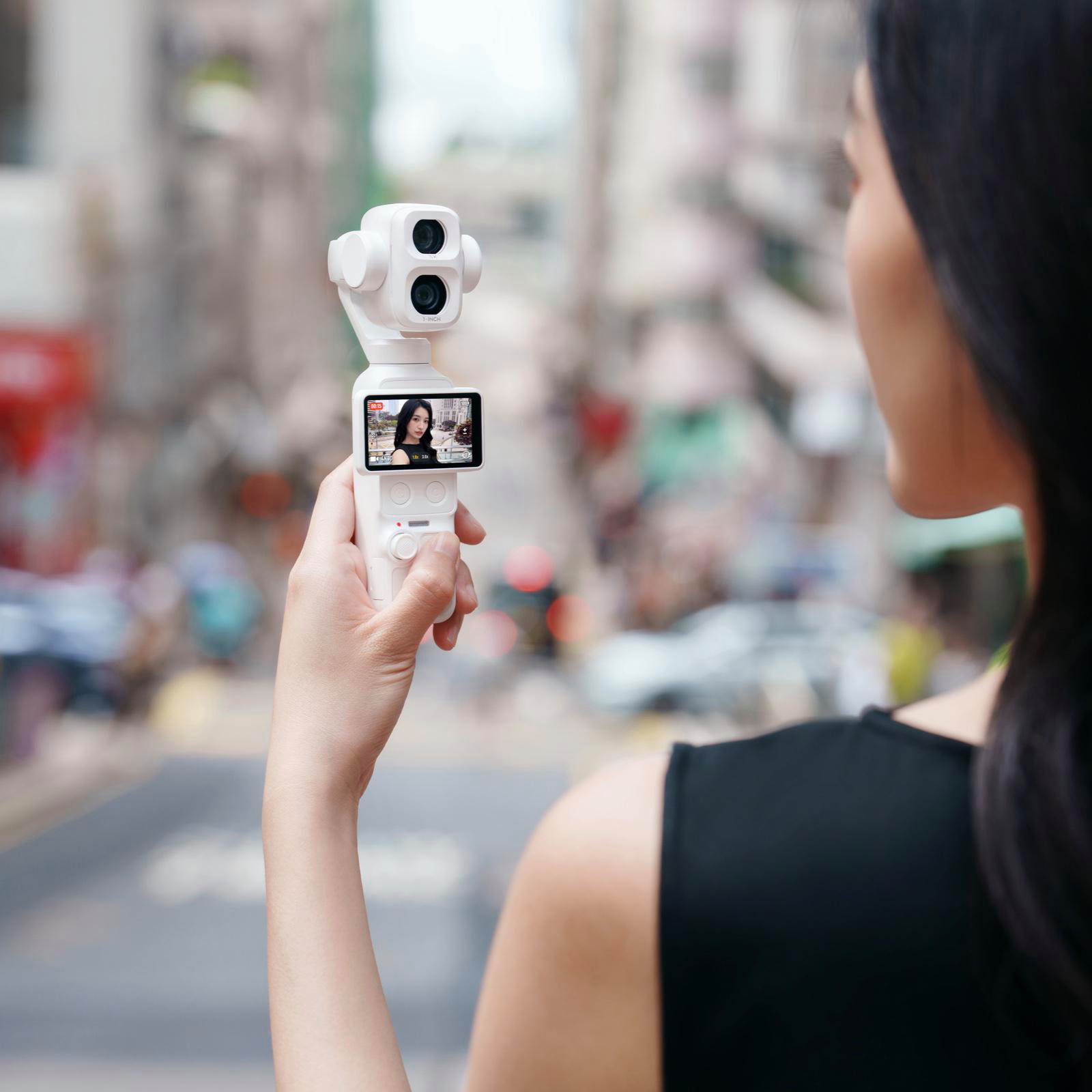 Eine Frau hält eine weiße Gimbal-Kamera in der Hand und filmt auf einer verschwommenen Straße.