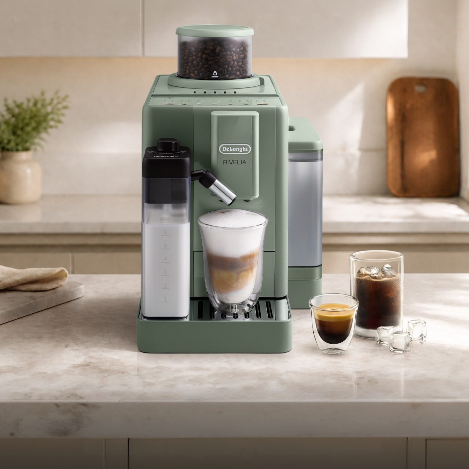 Una cafetera verde DeLonghi Rivelia sobre una encimera de cocina junto a vasos de café y leche.
