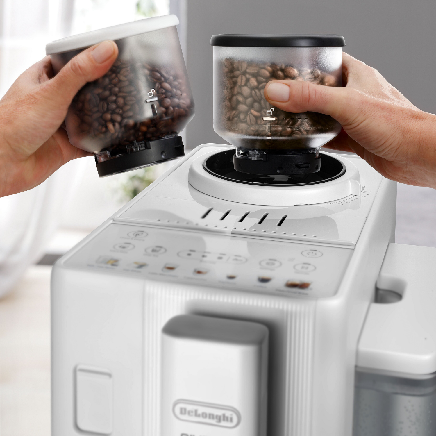 Unas manos colocan un recipiente de granos de café en una cafetera blanca.