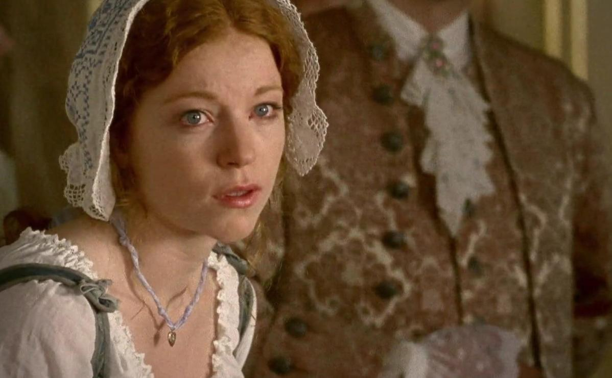 Eine Frau im historischen Kleid mit Spitzenhaube blickt besorgt neben einem Mann in formeller Kleidung.