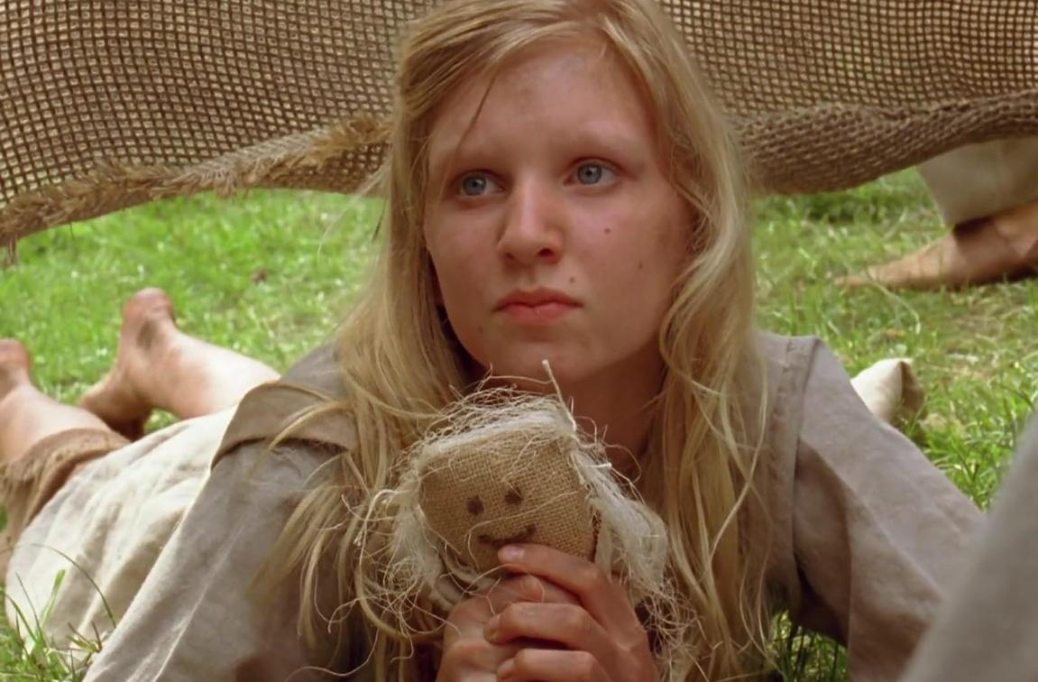 Ein junges blondes Mädchen liegt auf dem Gras und hält eine kleine Jutepuppe mit genähtem Gesicht.