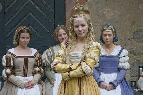 Vier Frauen in historischen Gewändern und Kopfbedeckungen stehen vor einer Wand und einer Holztür.