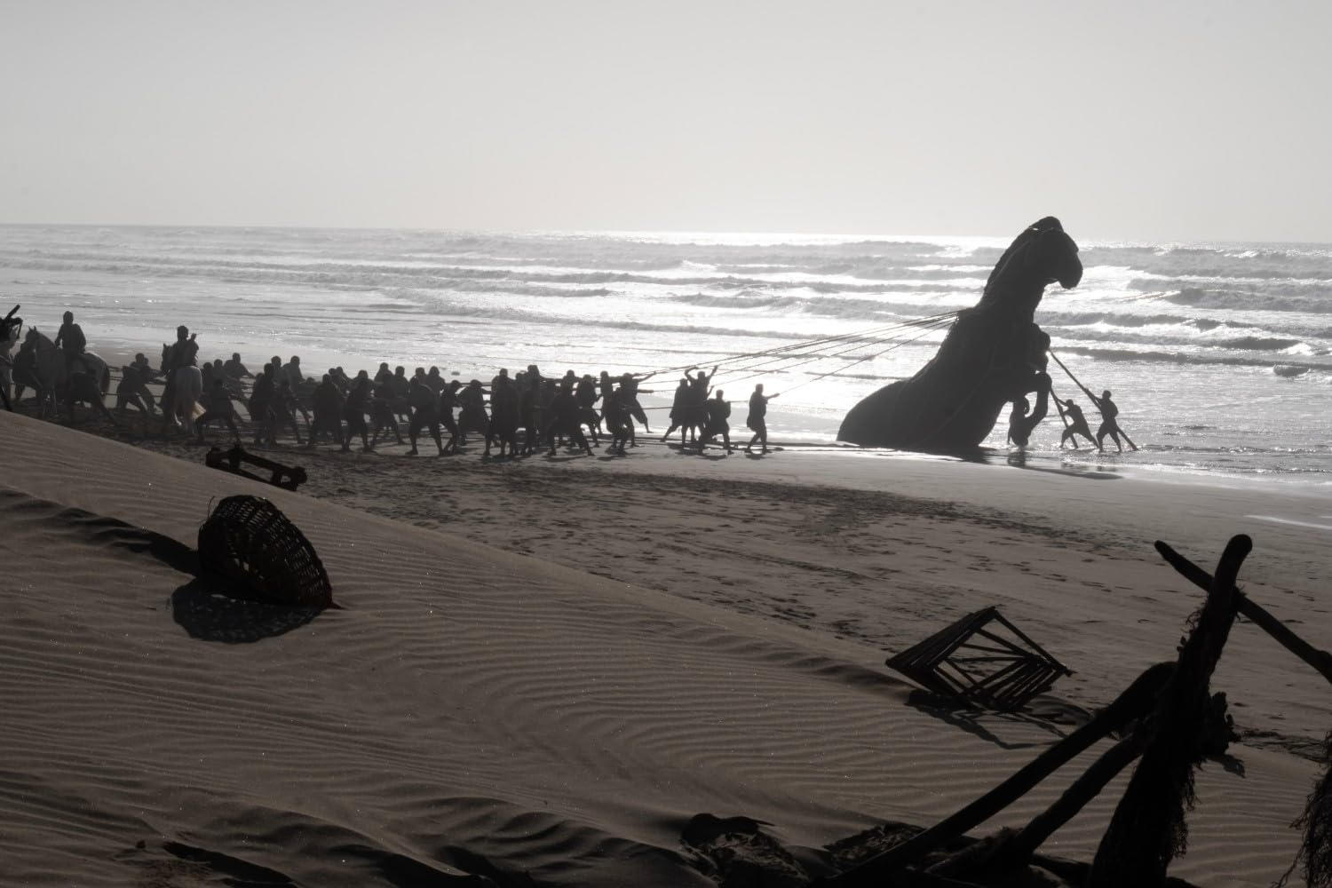 Eine Gruppe von Menschen zieht eine große pferdeähnliche Statue an einem sonnigen Strand aus dem Meer.