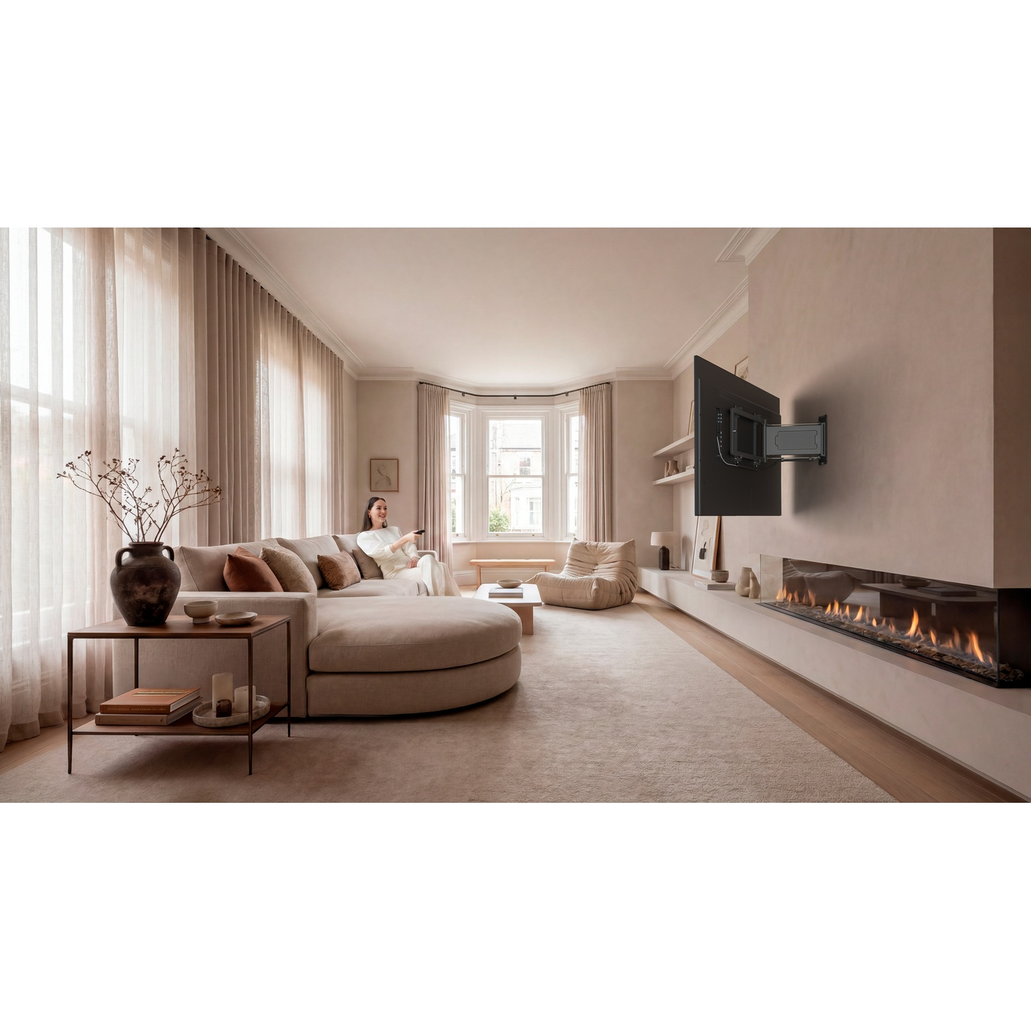 Een beige woonkamer met een vrouw op de bank, een tv aan de muur en een open haard.