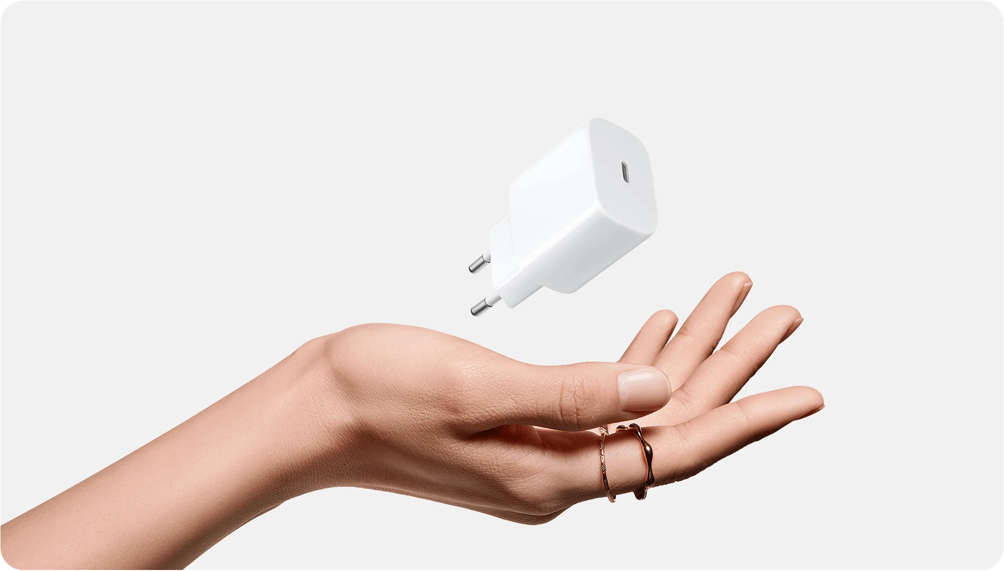 Egy nyitott kéz lebeg egy fehér USB-C töltő alatt világosszürke háttér előtt.