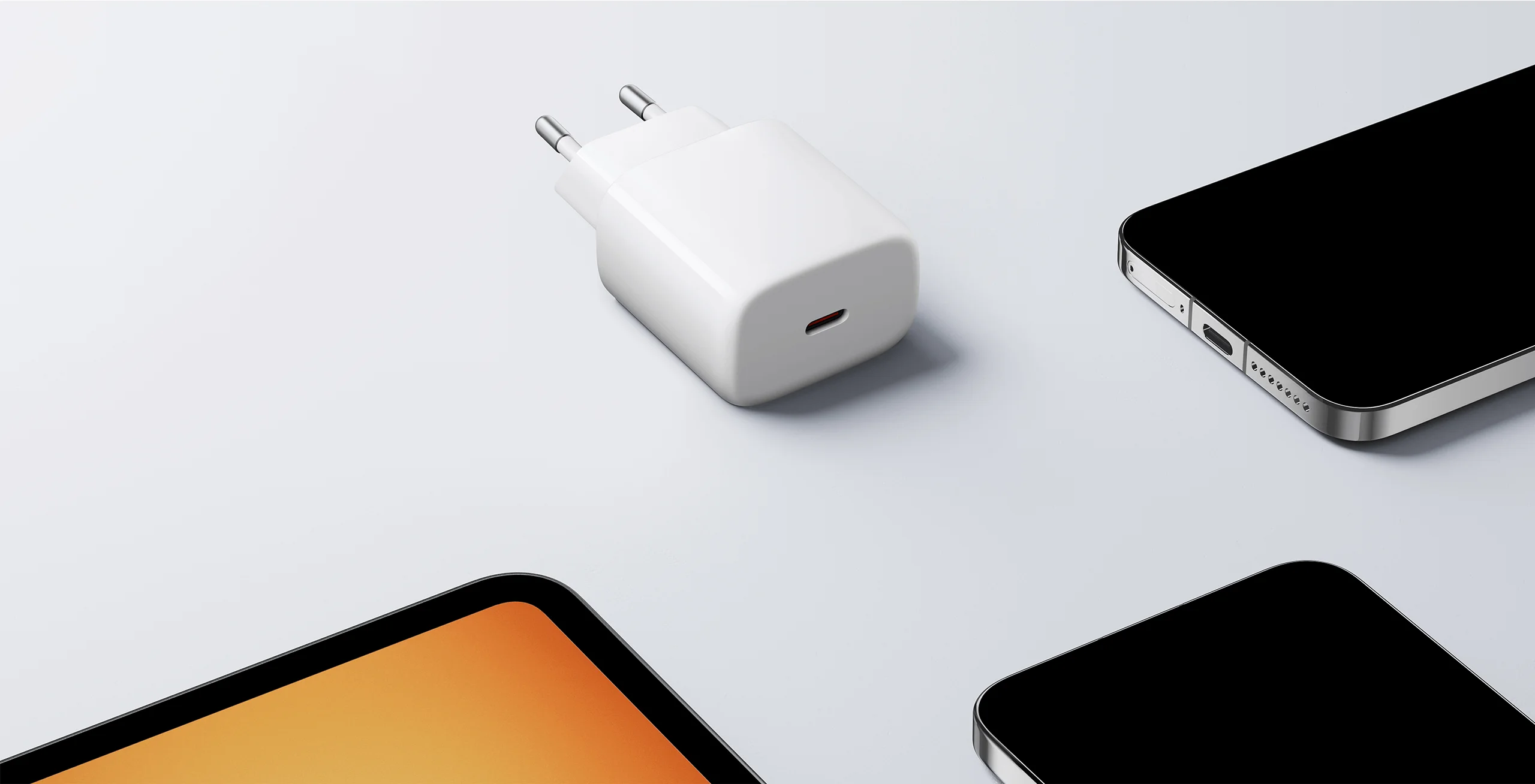 Egy fehér USB-C hálózati adapter fekszik egy világosszürke felületen két okostelefon mellett.
