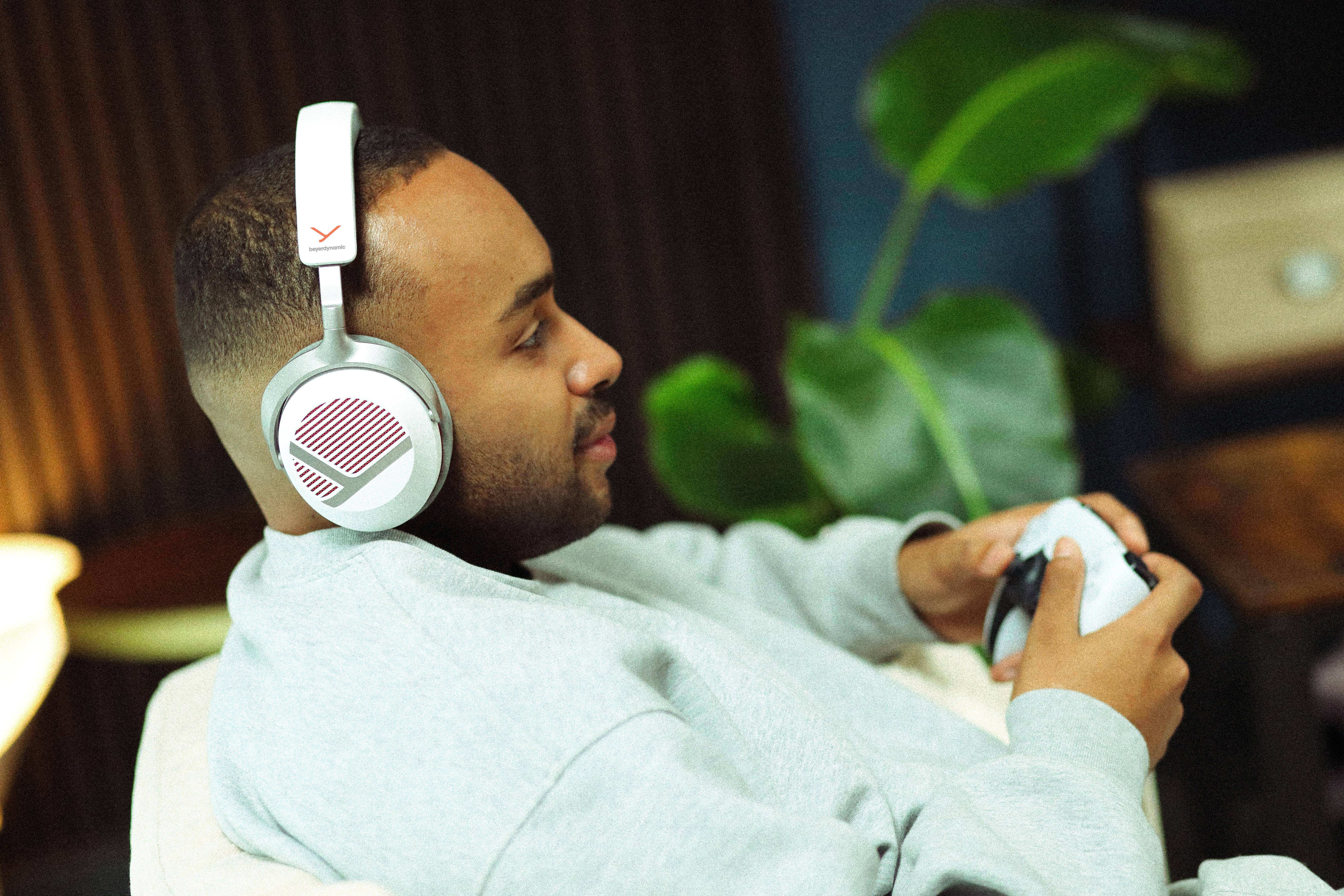 Ein junger Mann mit grauen Kopfhörern sitzt in einem Raum und hält einen weißen Controller in den Händen.