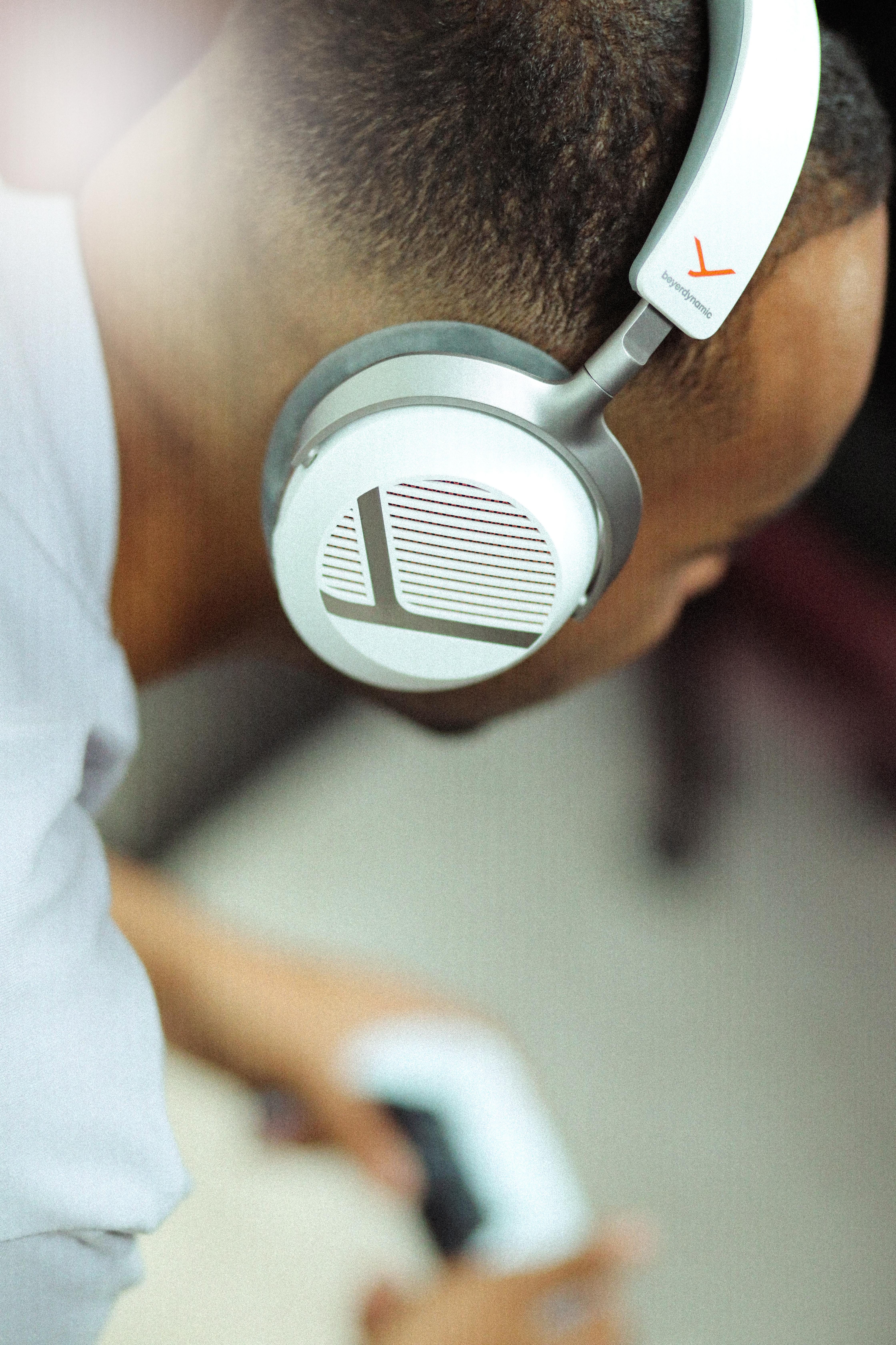Close-up of a person wearing white and silver Beyerdynamic headphones, looking down at a controller.
