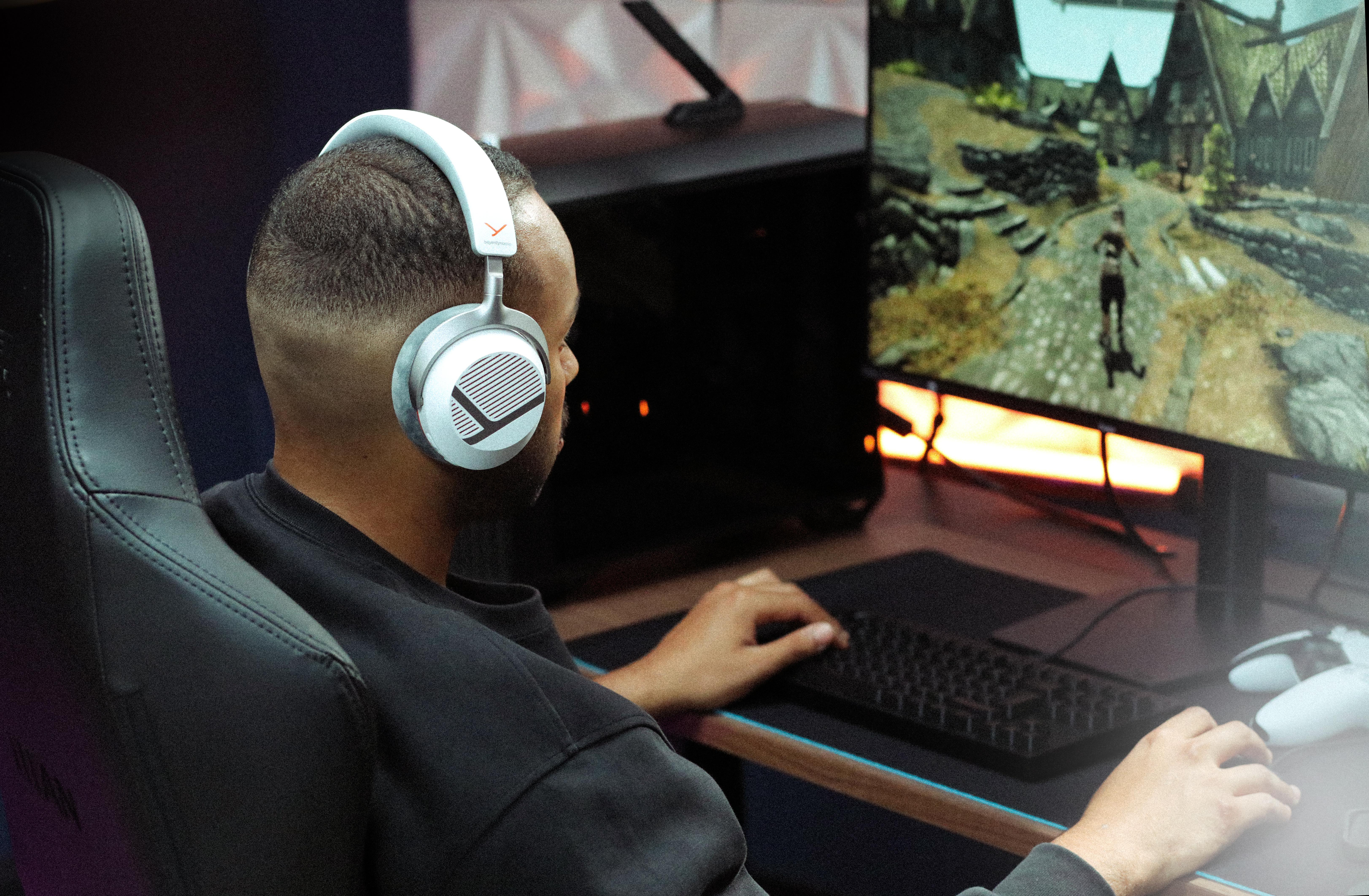 Ein Mann mit weißem Kopfhörer sitzt vor einem Monitor und spielt ein Videospiel.