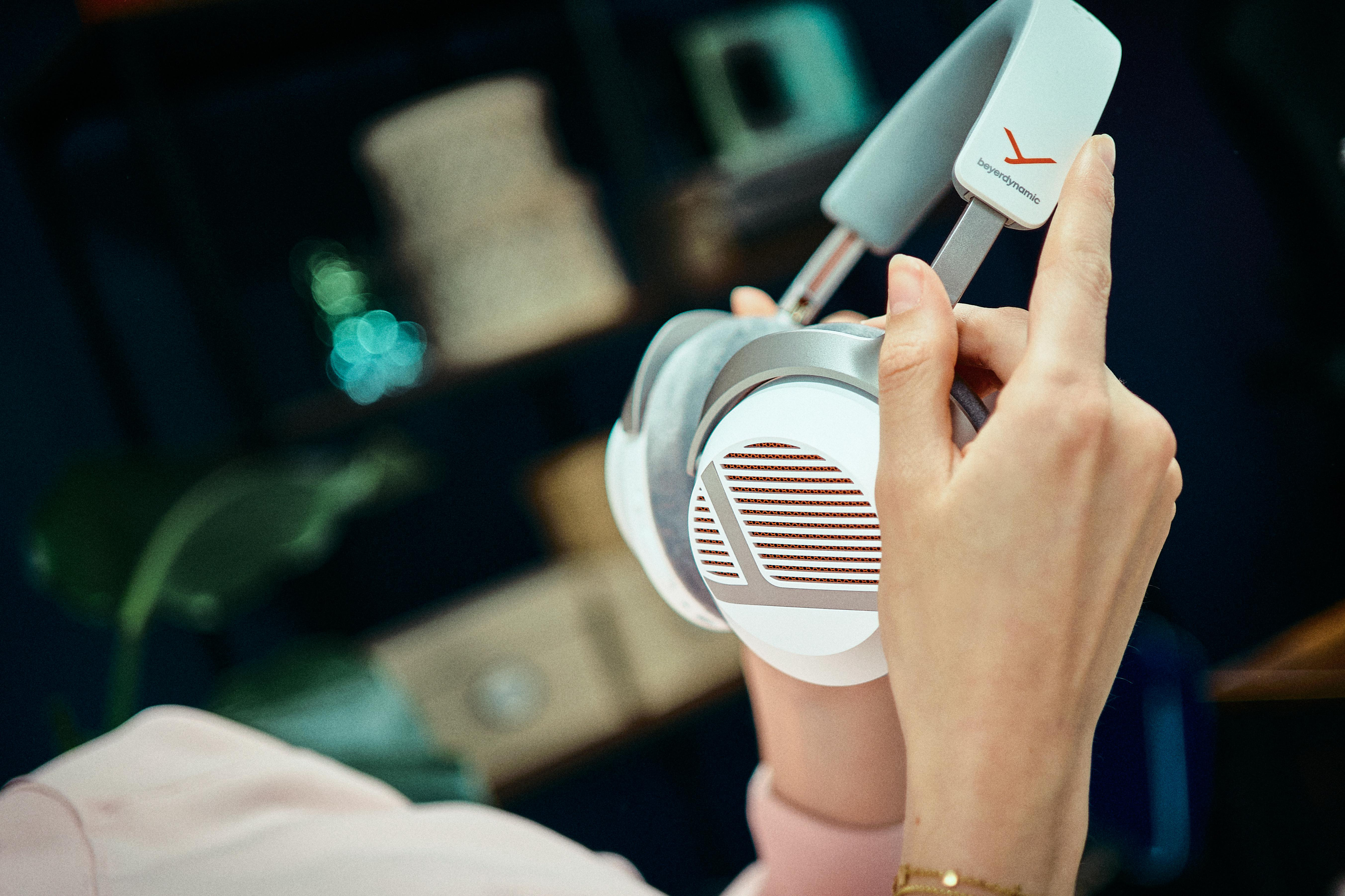 Jemand hält weiße und graue Beyerdynamic Kopfhörer in den Händen vor einem dunklen Hintergrund.