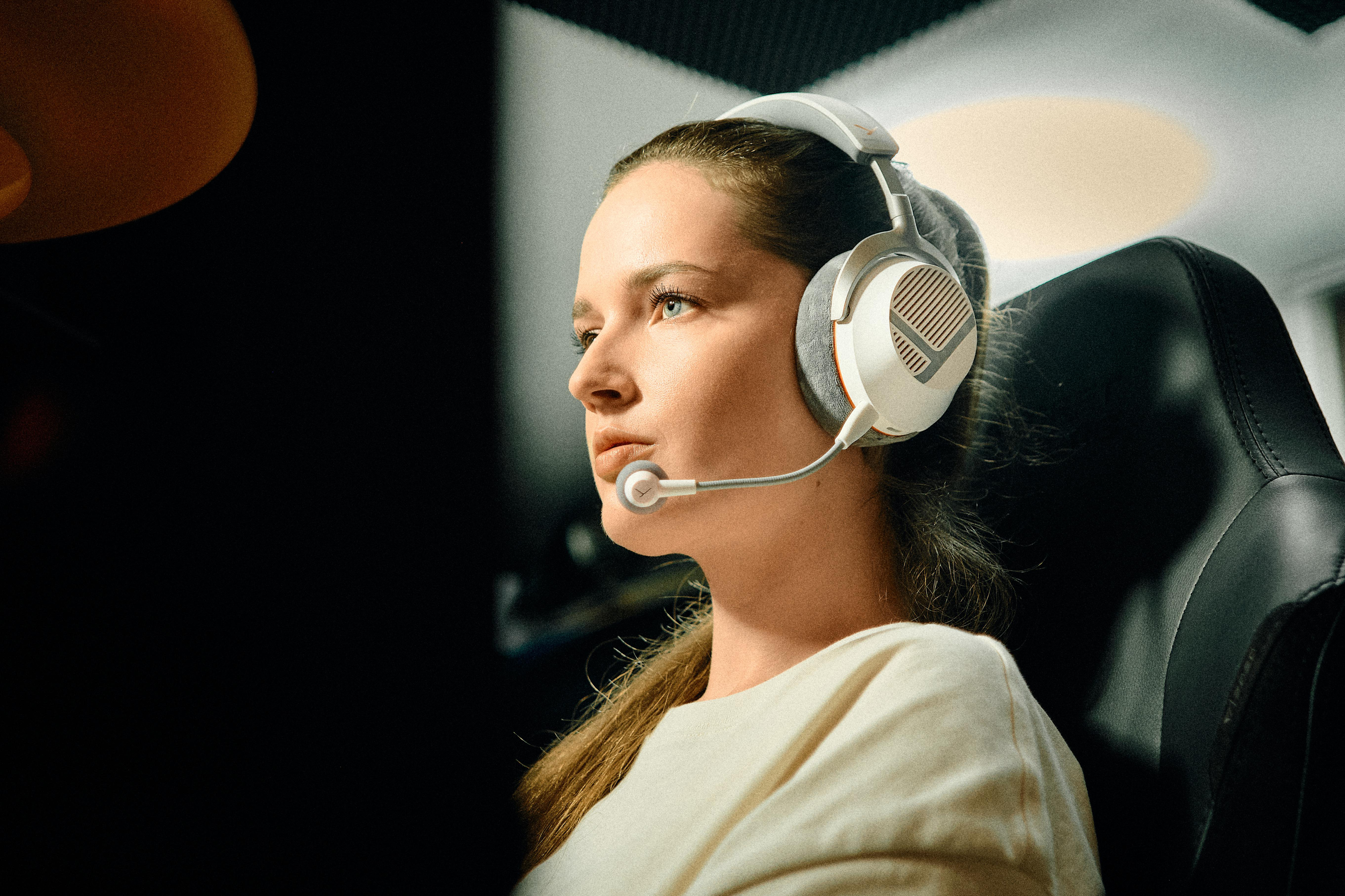 Frau mit weißem Headset sitzt in einem Gaming-Stuhl und schaut konzentriert nach links.